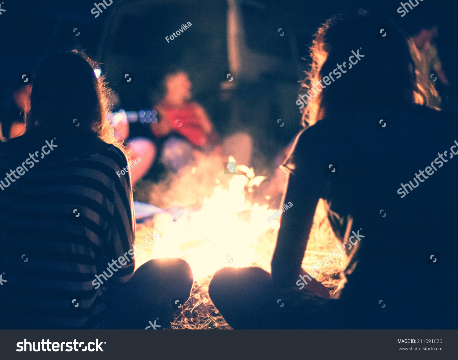 People sit at night round a bright bonfire