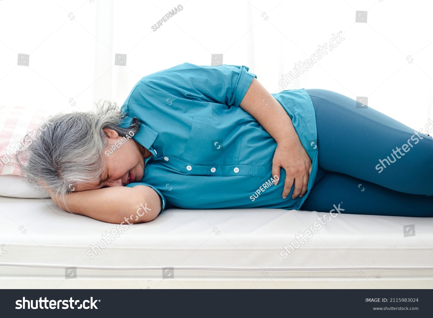 Asian elderly woman has a stomachache. She lay on the white bed. Elderly health concept. Health insurance and elderly care