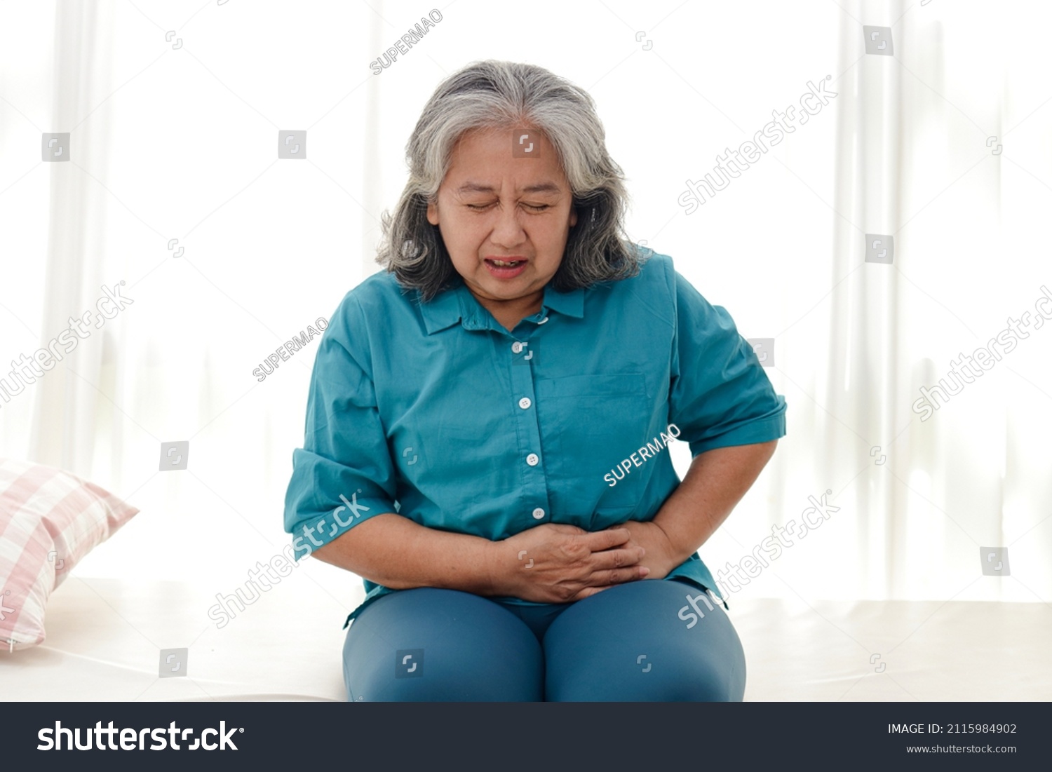 Asian elderly woman has a stomachache. She sat on the white bed. The concept of health care for the elderly. Illness. Health insurance.