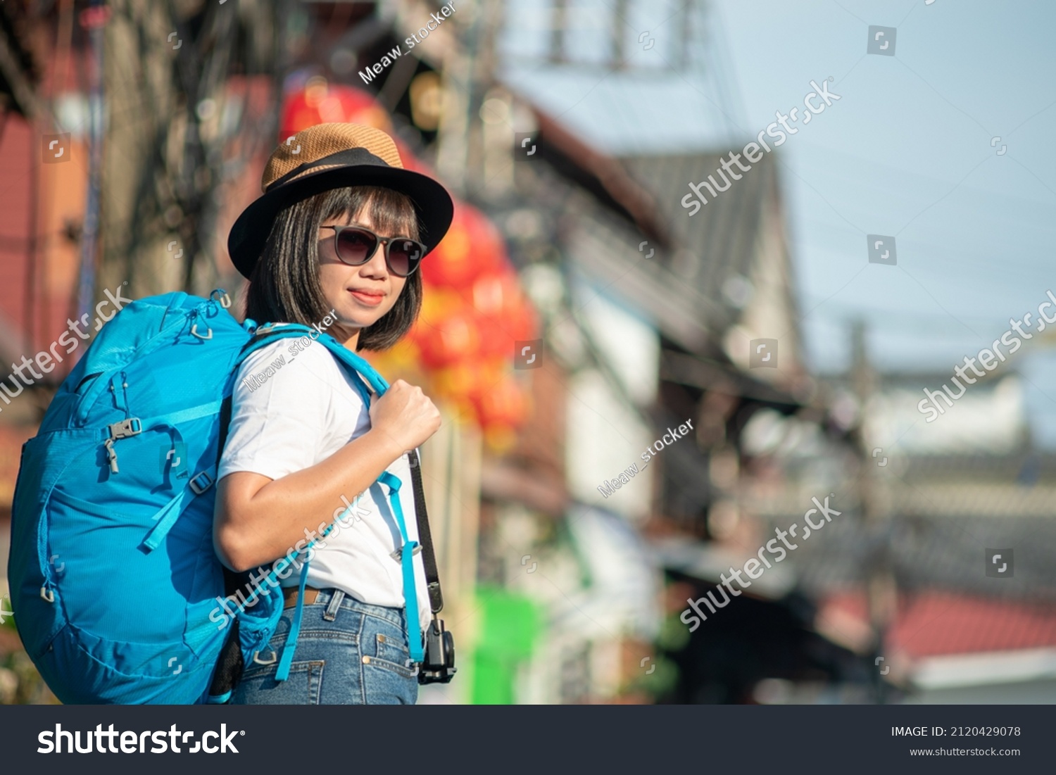 Asian woman walking travel backpack in city. Digital tourism concept. woman traveling with backpack and straw hat use smartphone to take pictures.