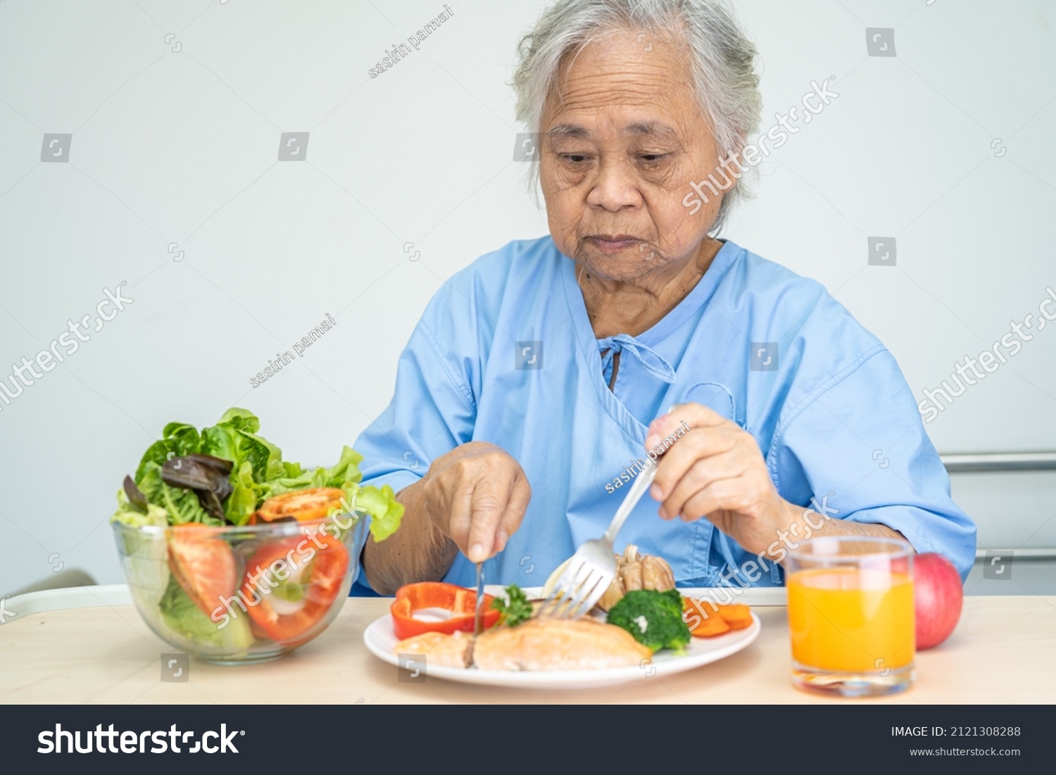 Asian senior or elderly old lady woman patient eating Salmon steak breakfast with vegetable healthy food while sitting and hungry on bed in hospital.