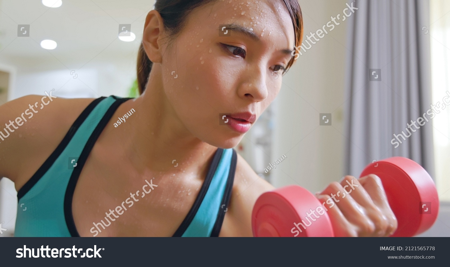 Beautiful athletic asian woman is sweating while training with dumbbell at home