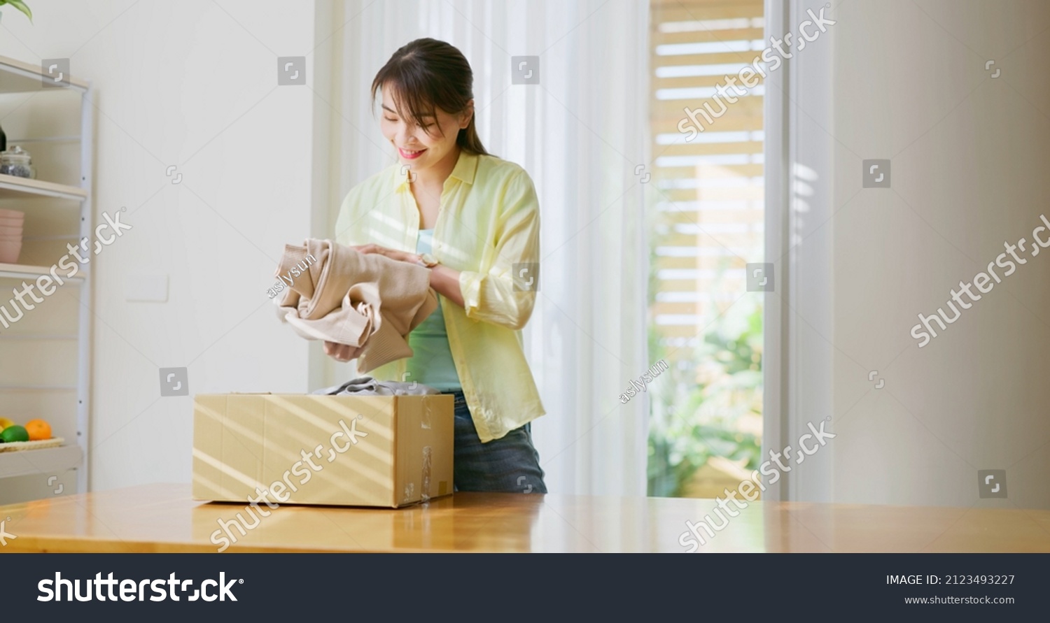 Asian woman is sort old clothes waste in garbage box for recycling at home