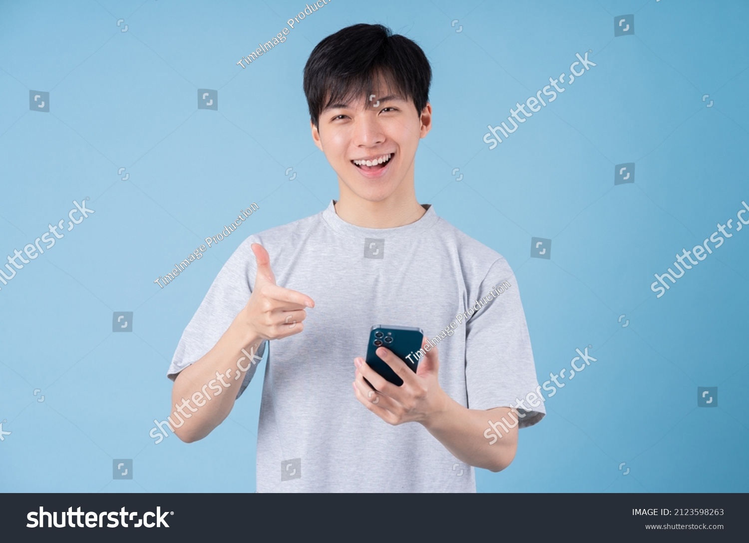 Young Asian man using smartphone on blue background