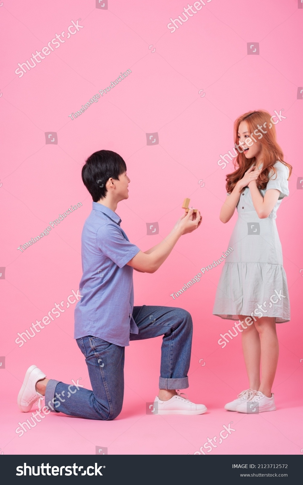 Young Asian man proposes to his girlfriend on a pink background
