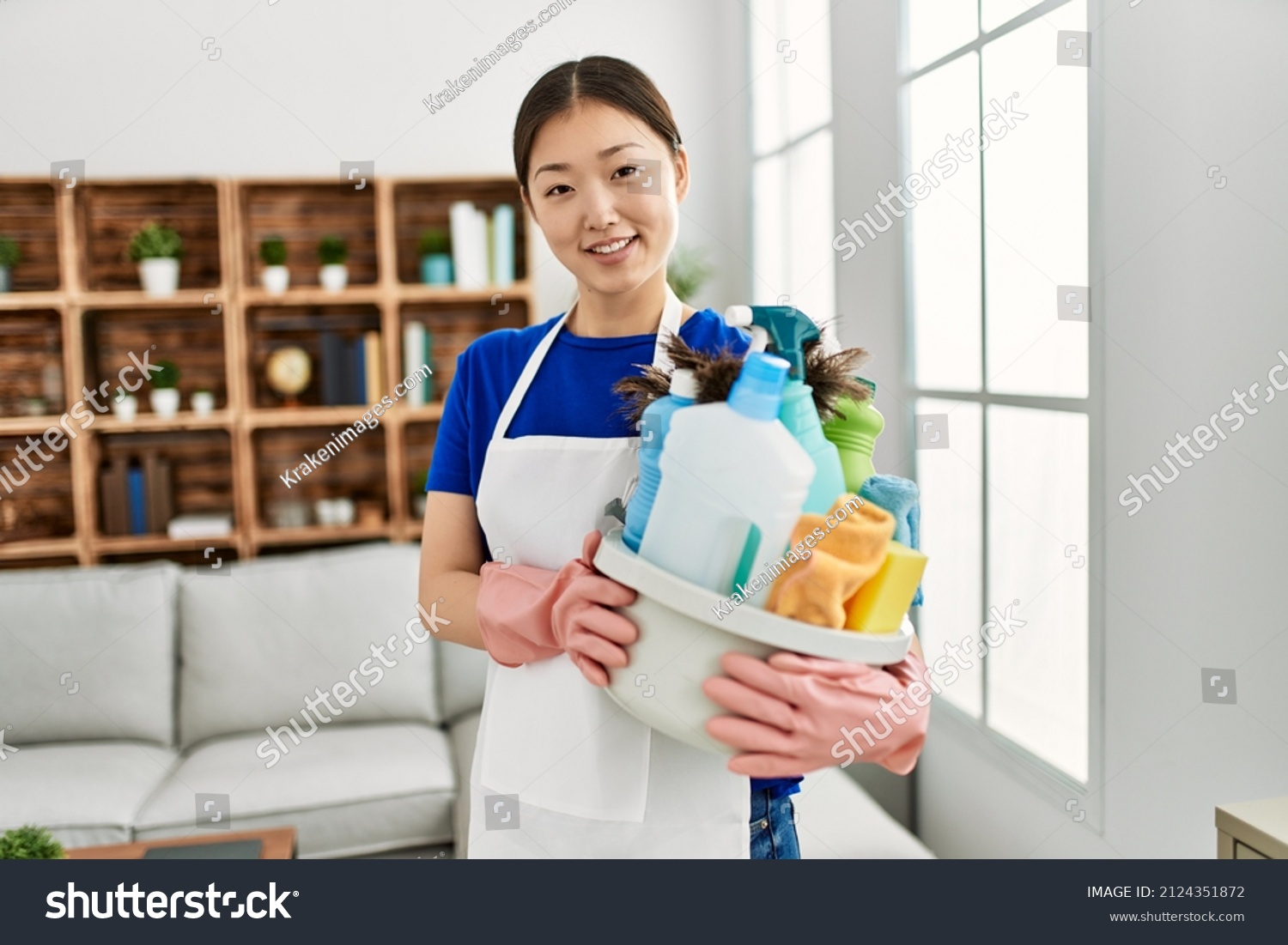 Young chinese housewife holding cleaning products standing at home.