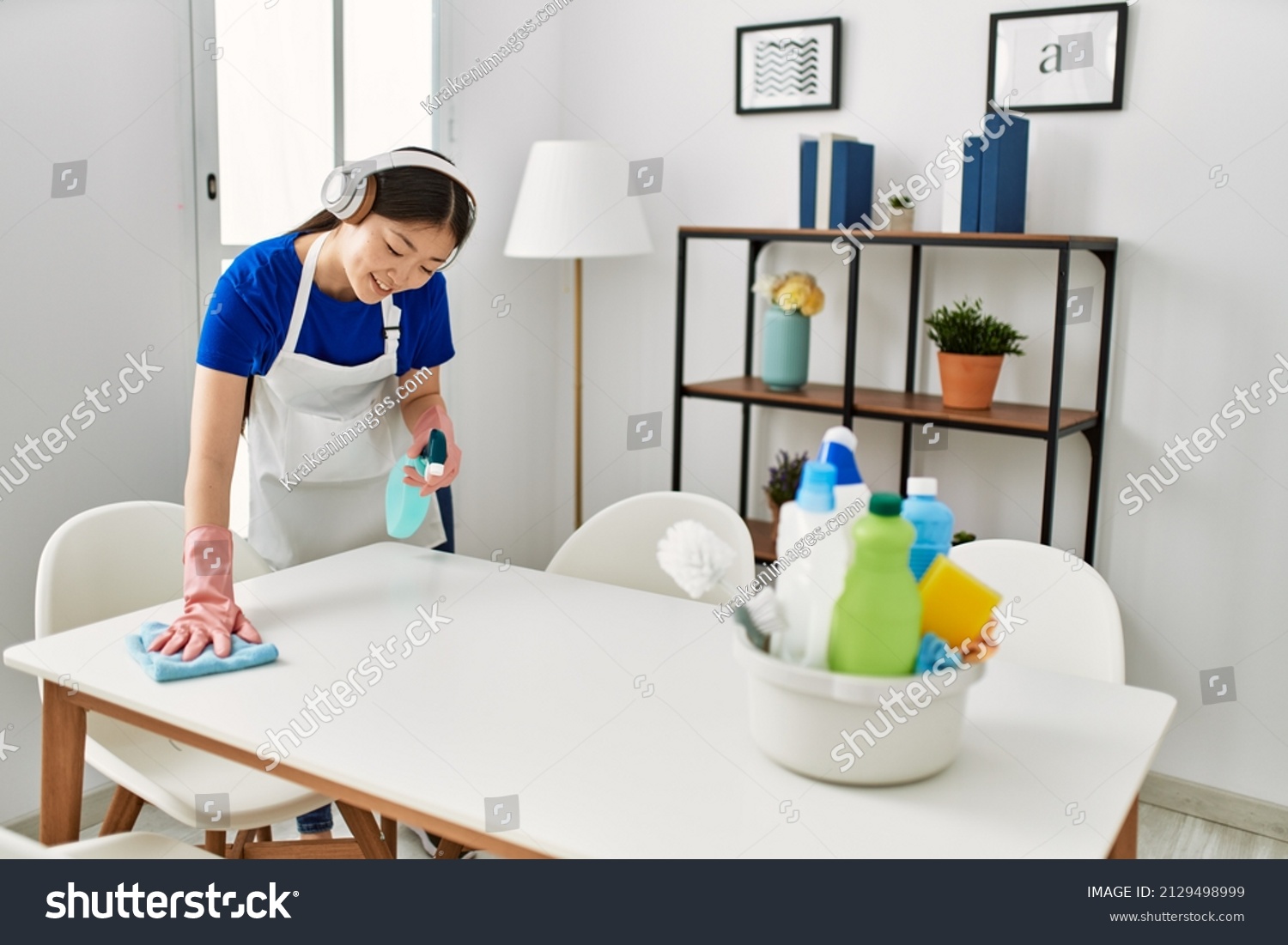 Young chinese housewife cleaning and listening to music using headphones at home.