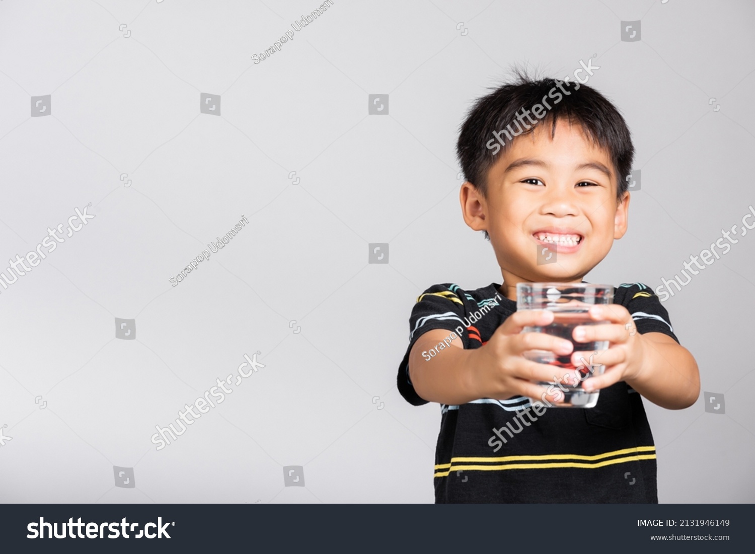 Little cute kid boy 5-6 years old smile drinking fresh water from glass in studio shot isolated on white background  Asian children preschool  Daily life health