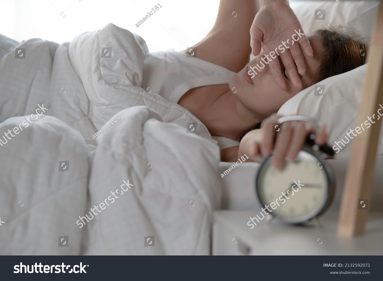 Woman turning off alarm clock in bedroom in the morning