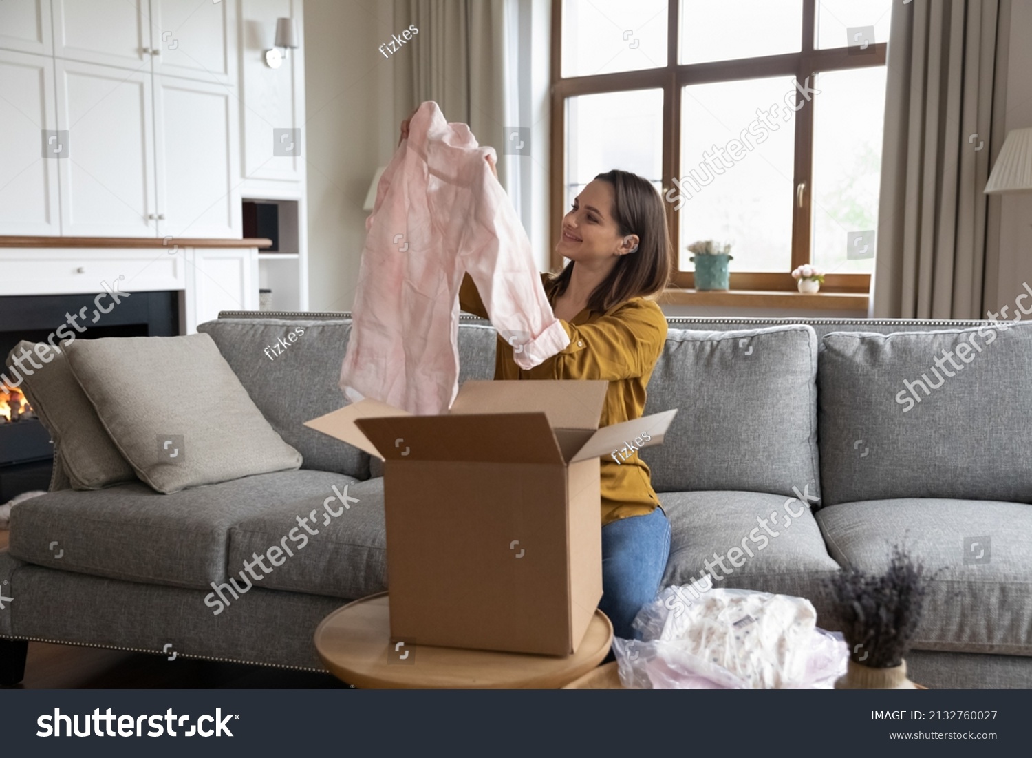 Smiling woman unpack parcel box with delivered online fashion store clothes check blouse quality feel satisfied by received apparels. Client of e-commerce webstore express delivery services concept