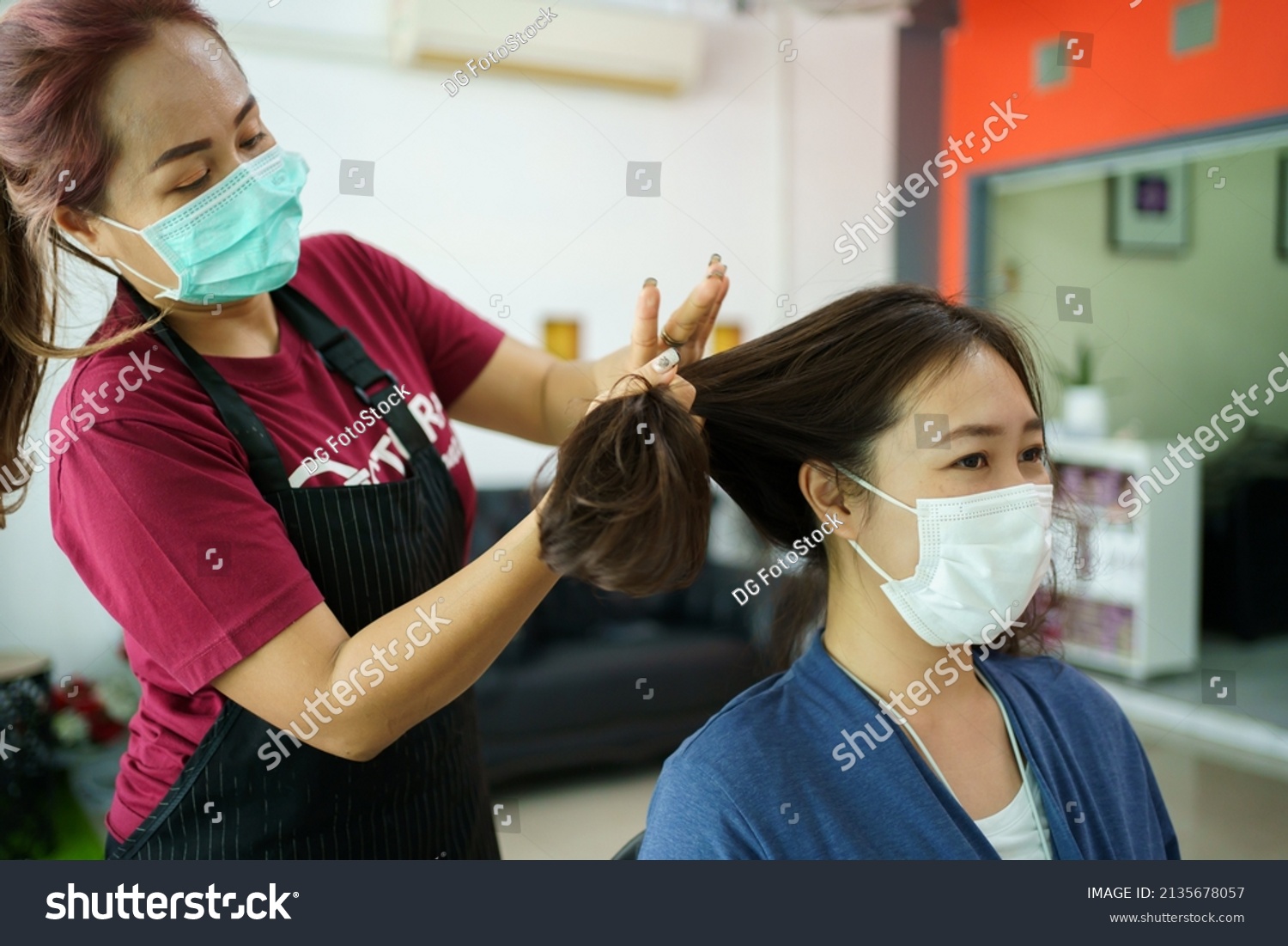 Asian young woman have a hair cutting and spa by professional beauty hair dresser. Woman sitting on the chair in beauty - Salon shop while barber cutting her hair.