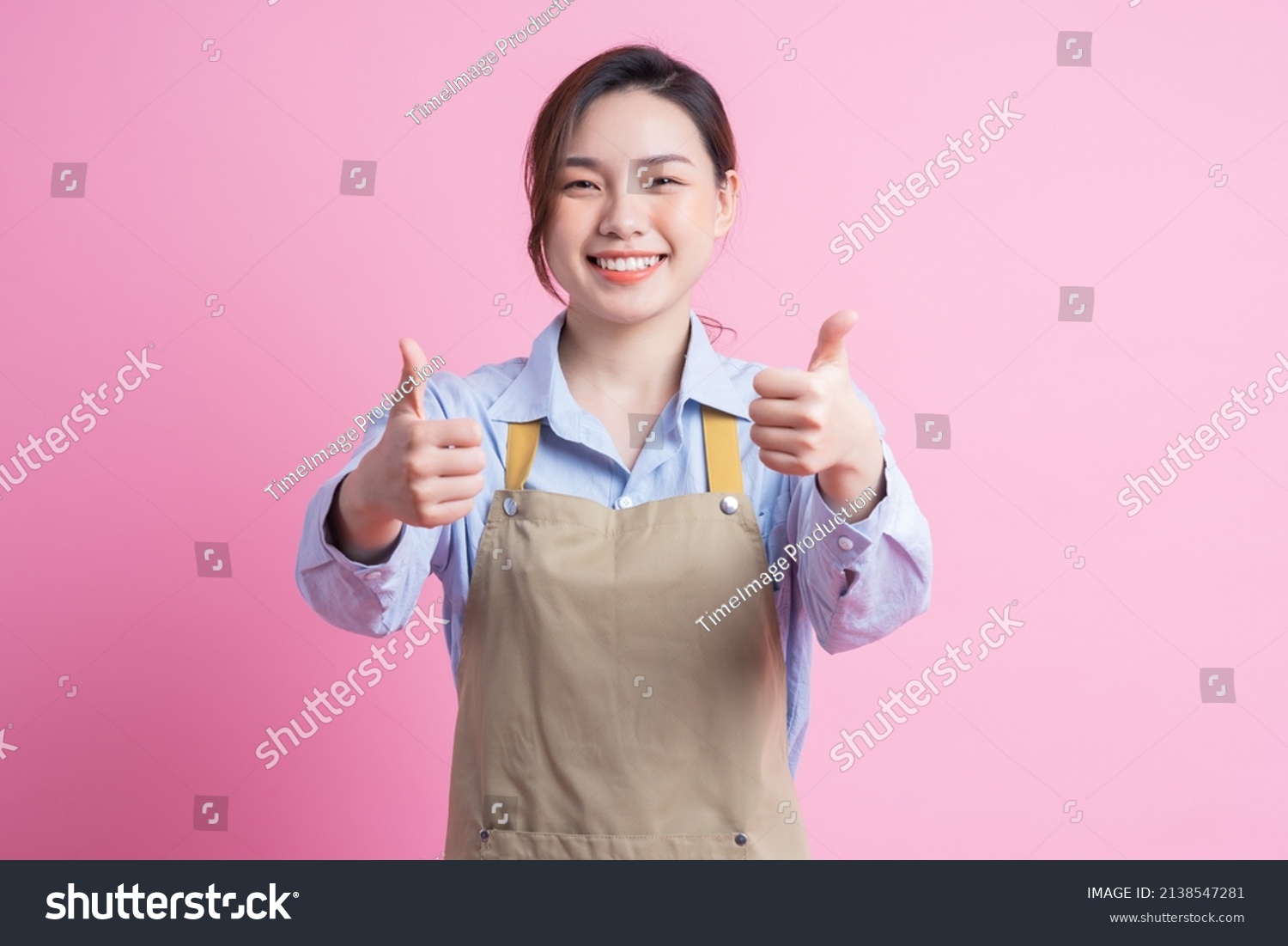 Young Asian waitress standing on pink background