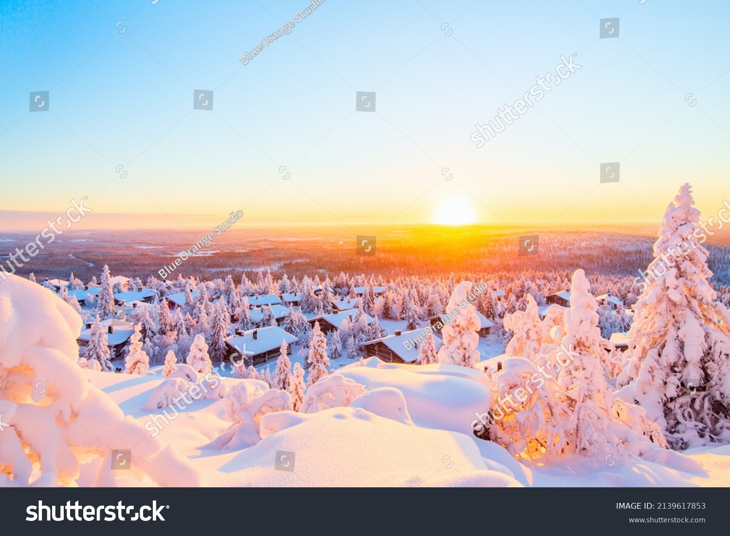 Stunning sunset view over wooden huts and snow covered trees in Finnish Lapland