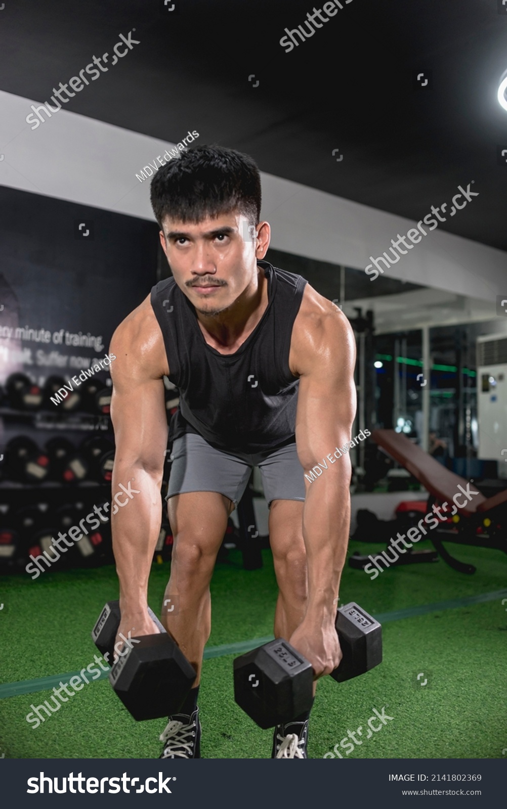 A fit asian man does bent-over dumbbell rows. Weight and resistance training at the gym.
