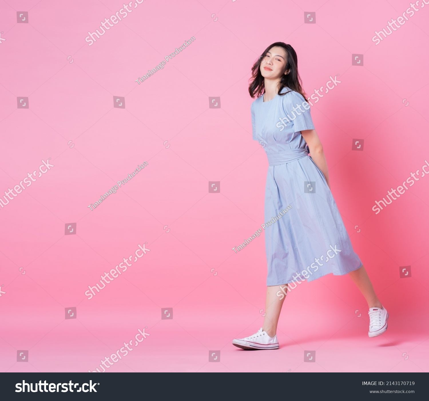 Full length image of young Asian woman wearing blue dress on pink background