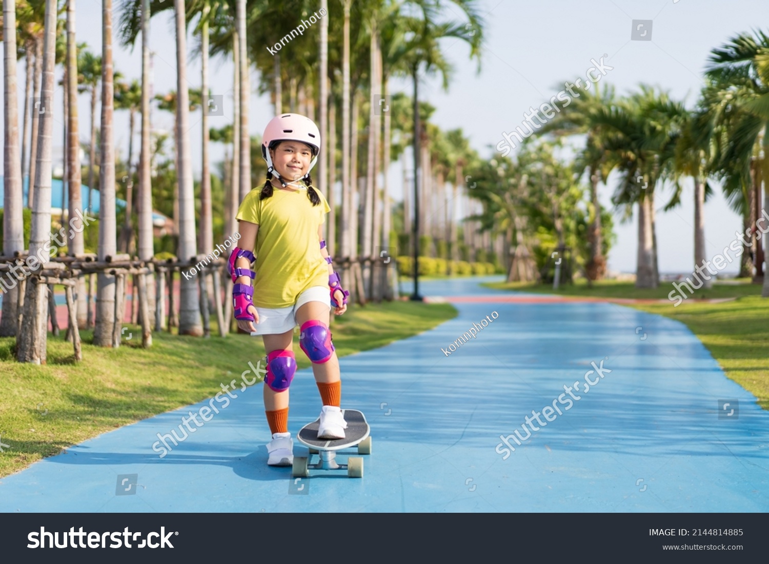 asian child or kid girl playing skateboard or surf skate in skating rink track and extreme sports exercise to wearing helmet elbow pads wrist and knee support for body safety protect at bang phra park