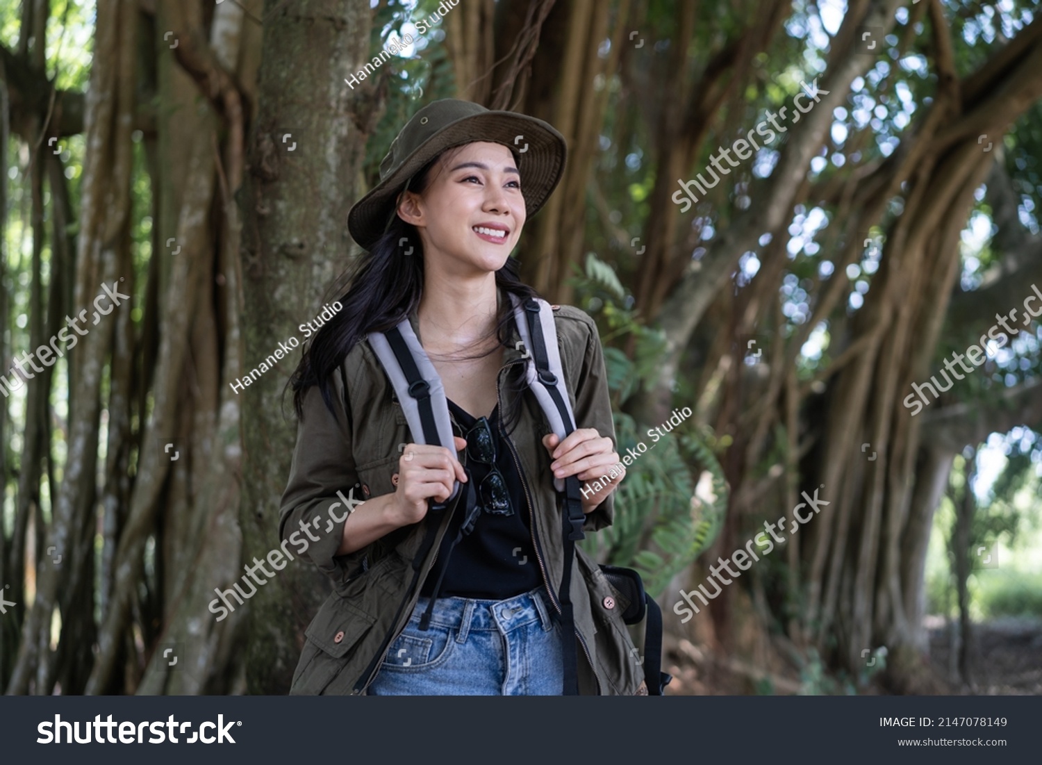 Asian young beautiful female backpacker traveling alone in forest wild. Attractive girl traveler look around and explore while walk in nature wood with happiness and fun during holiday vacation trip.