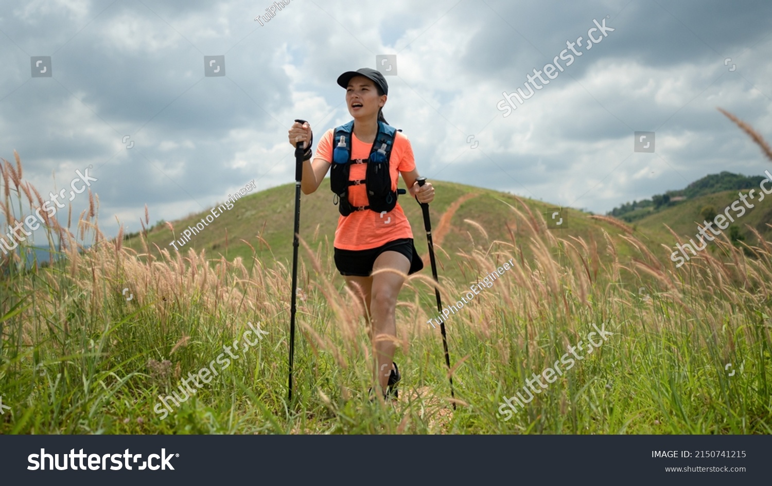 Young women active trail running across a meadow on a grassy trail high in the mountains in the afternoon with trekking pole