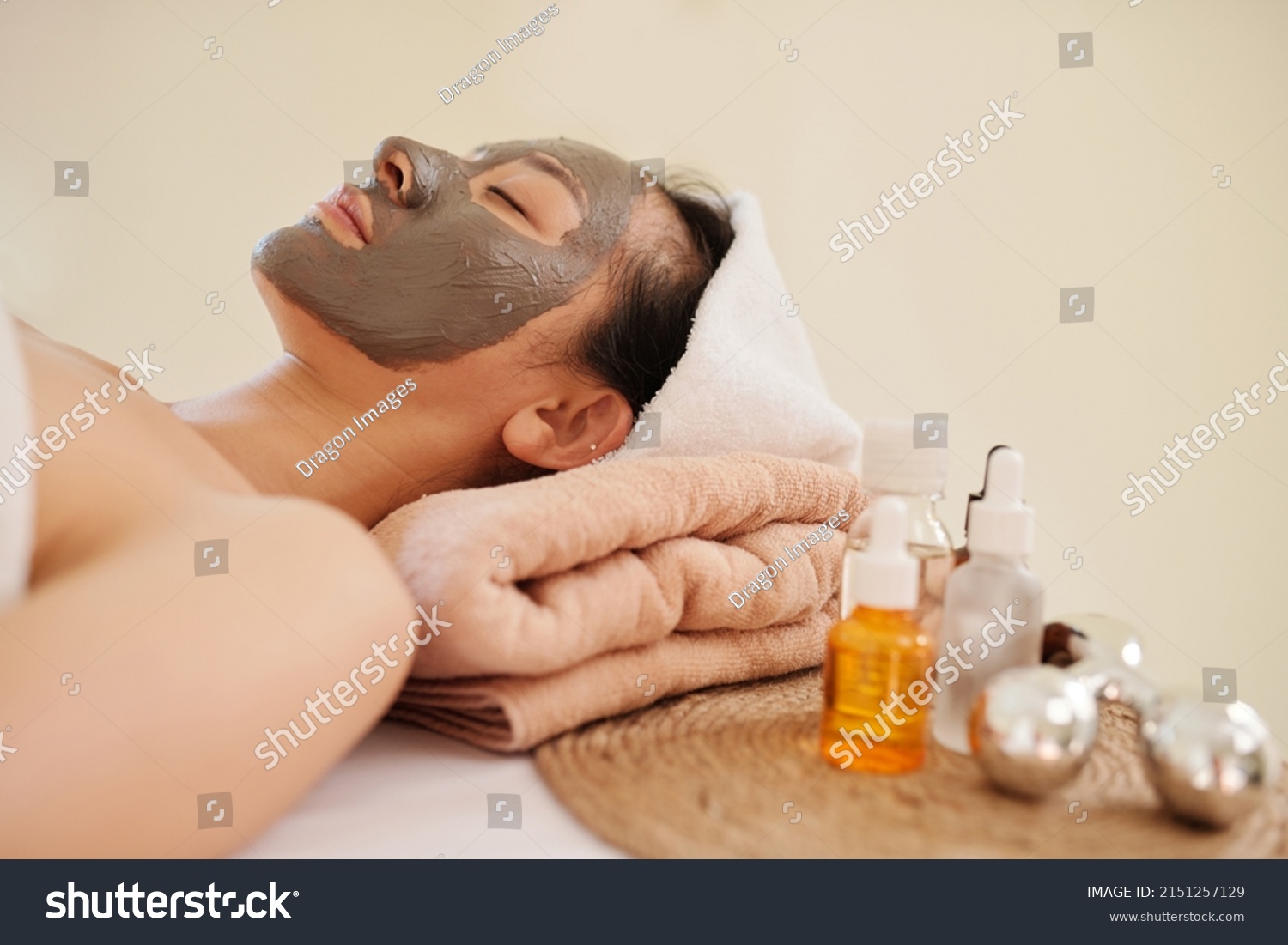 Young Asian woman relaxing on bed in spa salon with pore clearing clay mask on face