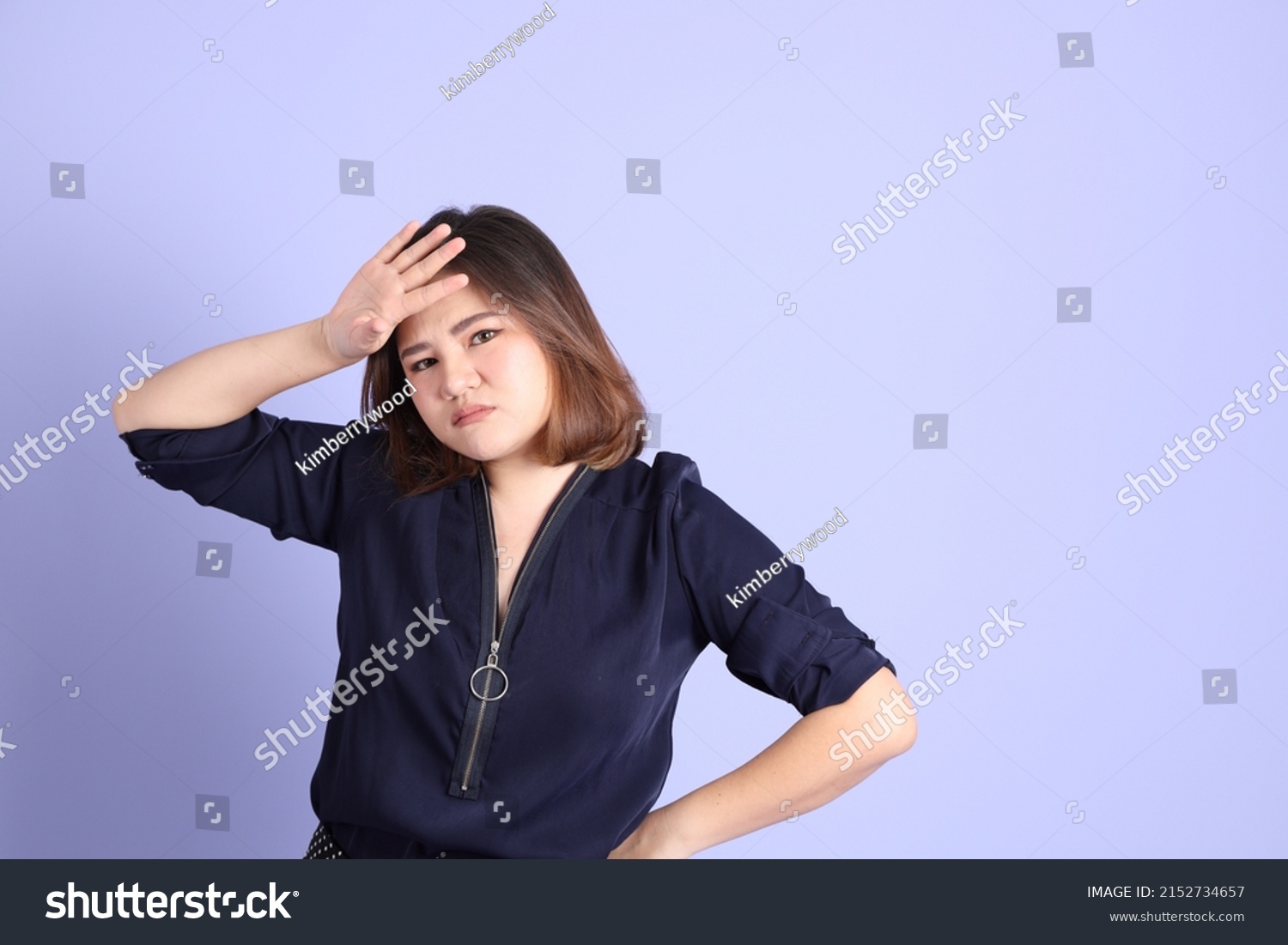 The chubby Asian woman standing on the purple background with the casual clothes.