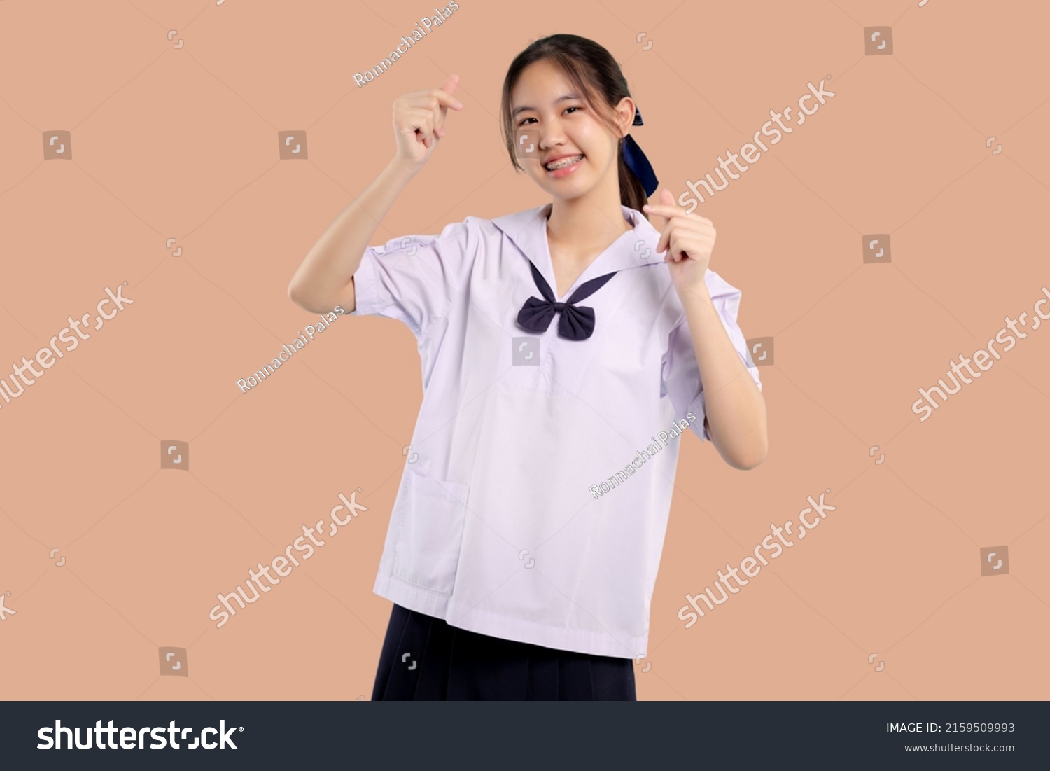 Happy braces Asian student girl in school uniform smiling on isolated pastel background.