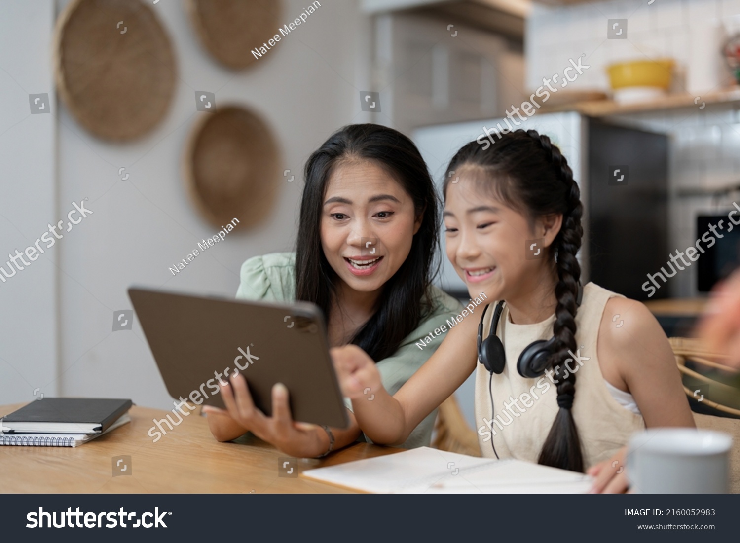 portrait of cheerful asian mother and daughter using digital tablet in kitchen at home