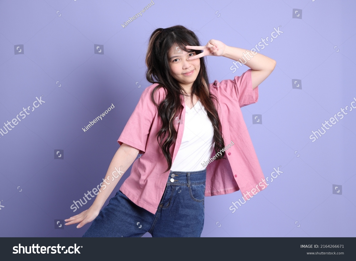 The cute young Asian girl with casual clothes standing on the purple background.