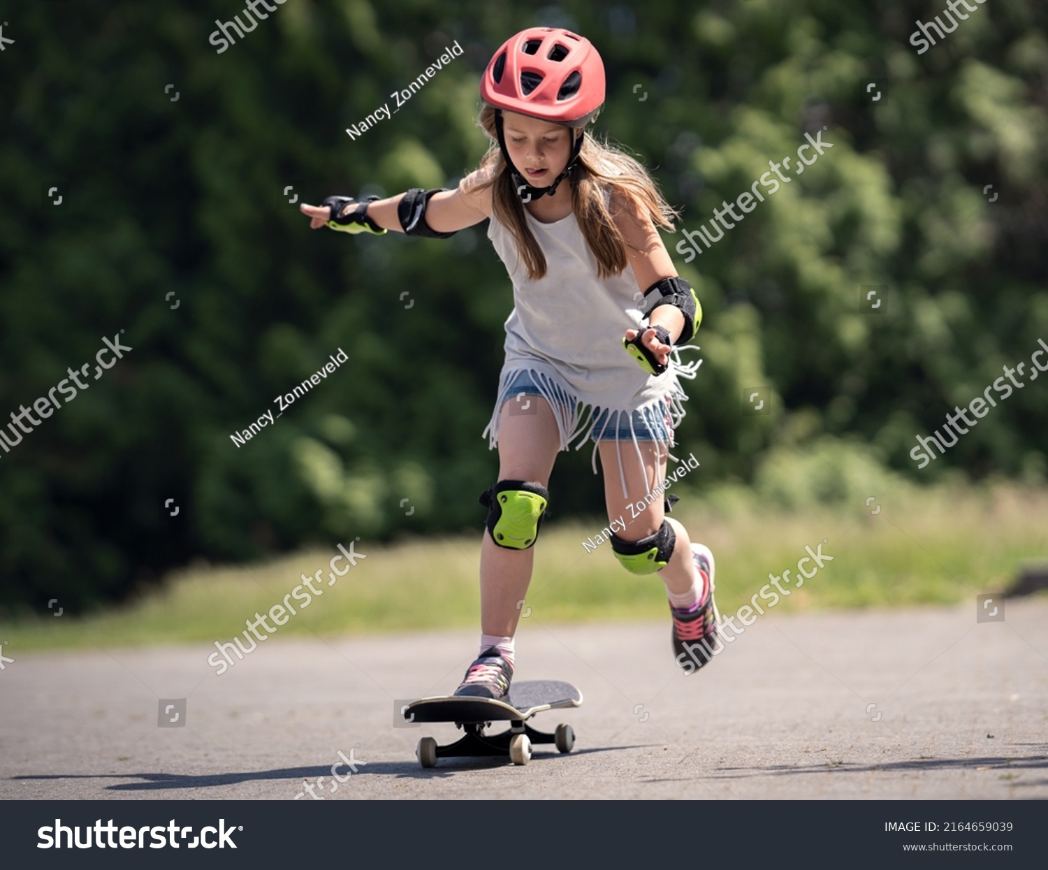 Girl (8 year old) with helmet and protection gear skate boarding outside in the park in the summer. Child on skate board.