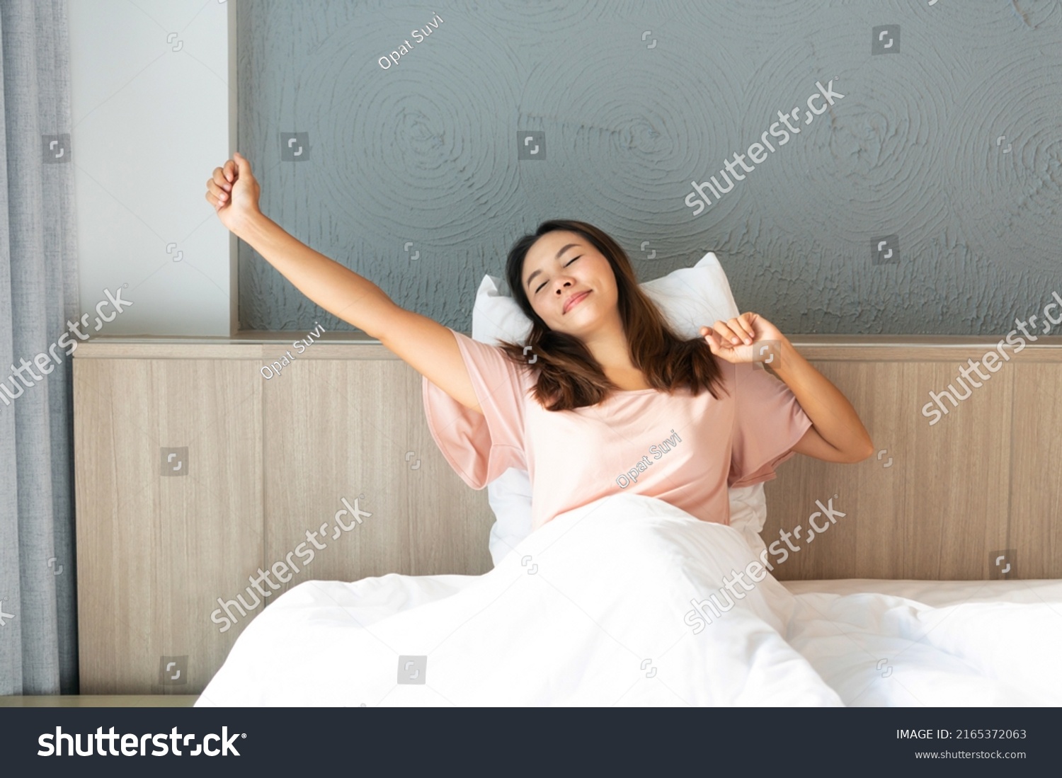 Smiling young Asian woman stretching after wake up with sunrise in the morning in bedroom at home.