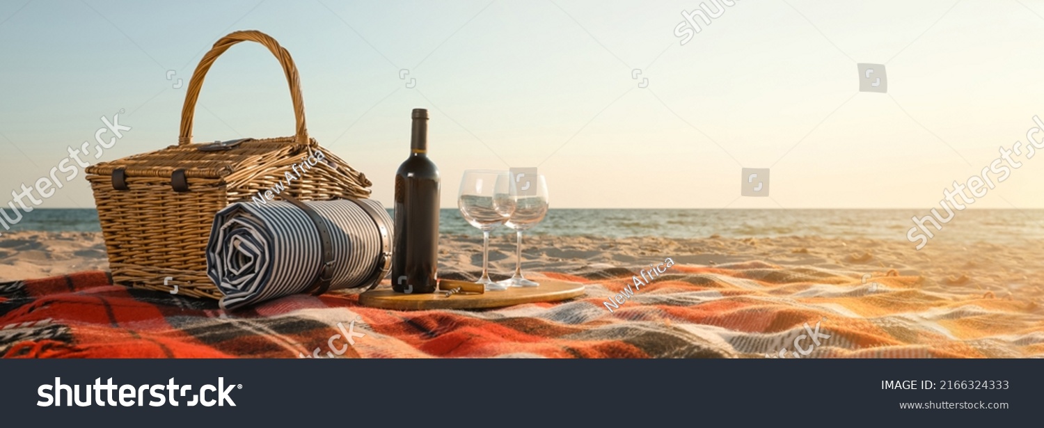 Blanket with picnic basket bottle of wine and glasses on sandy beach ...