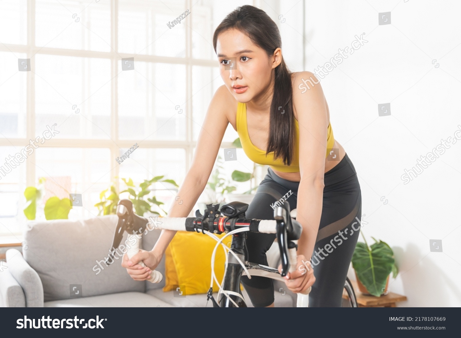 Cardio fitness  athlete cyclist asian young woman in sportswear bike indoors  online bicycle cycling on trainer in living room at home. Exercise training for healthy body strong athletic  fit active.