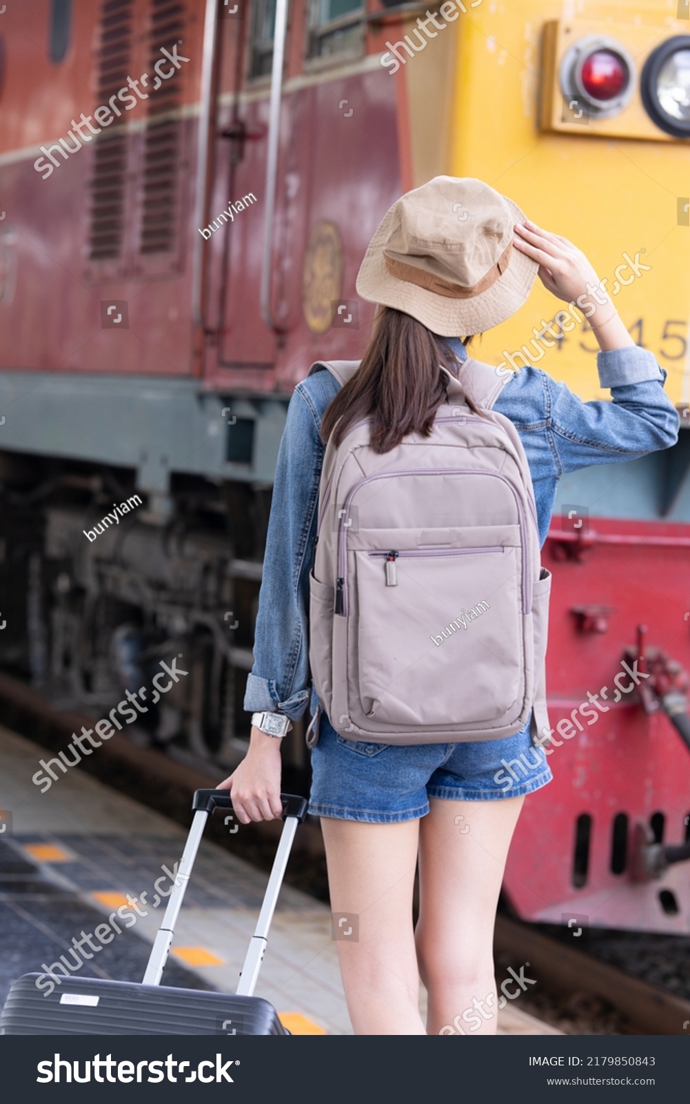 Young asian woman traveler with backpack in the railway Backpack and hat at the train station with a traveler Travel concept. Woman traveler tourist walking at train station
