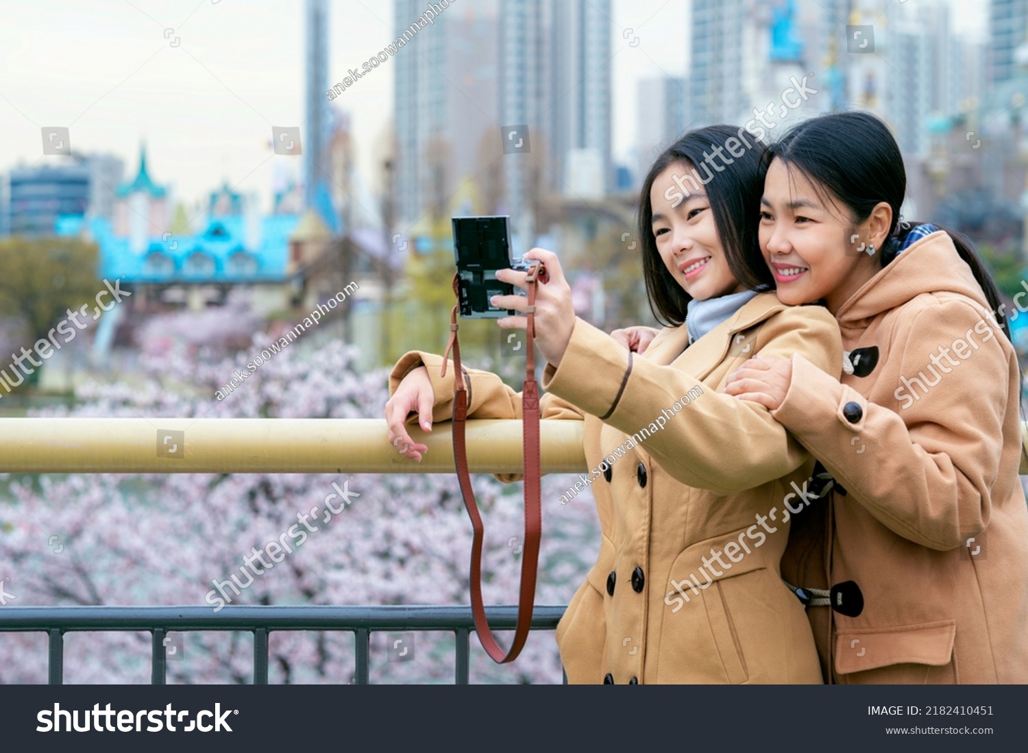 Asian woman traveler mother and her daughter take selfie togather at view point in Seoul city South Korea in winter season with cherry blossom background