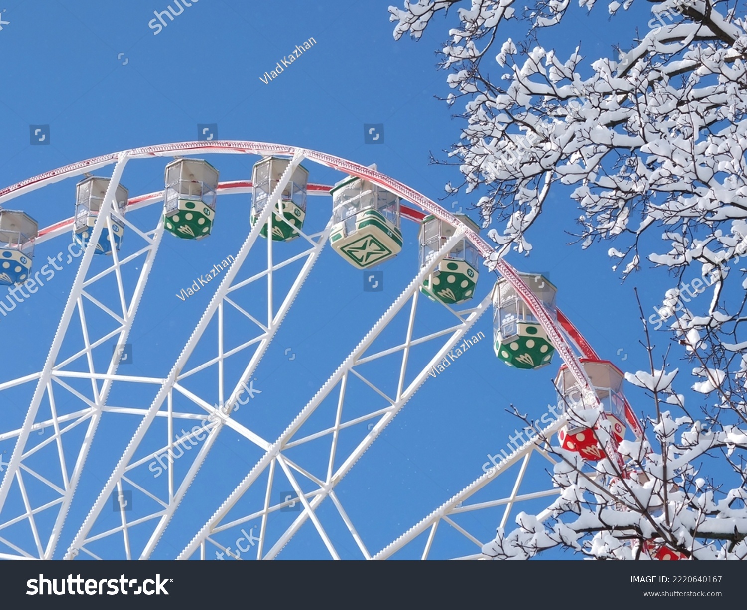 Ferris wheel in winter against the blue sky. Snow on the branches of a tree. Kharkiv city Ukraine