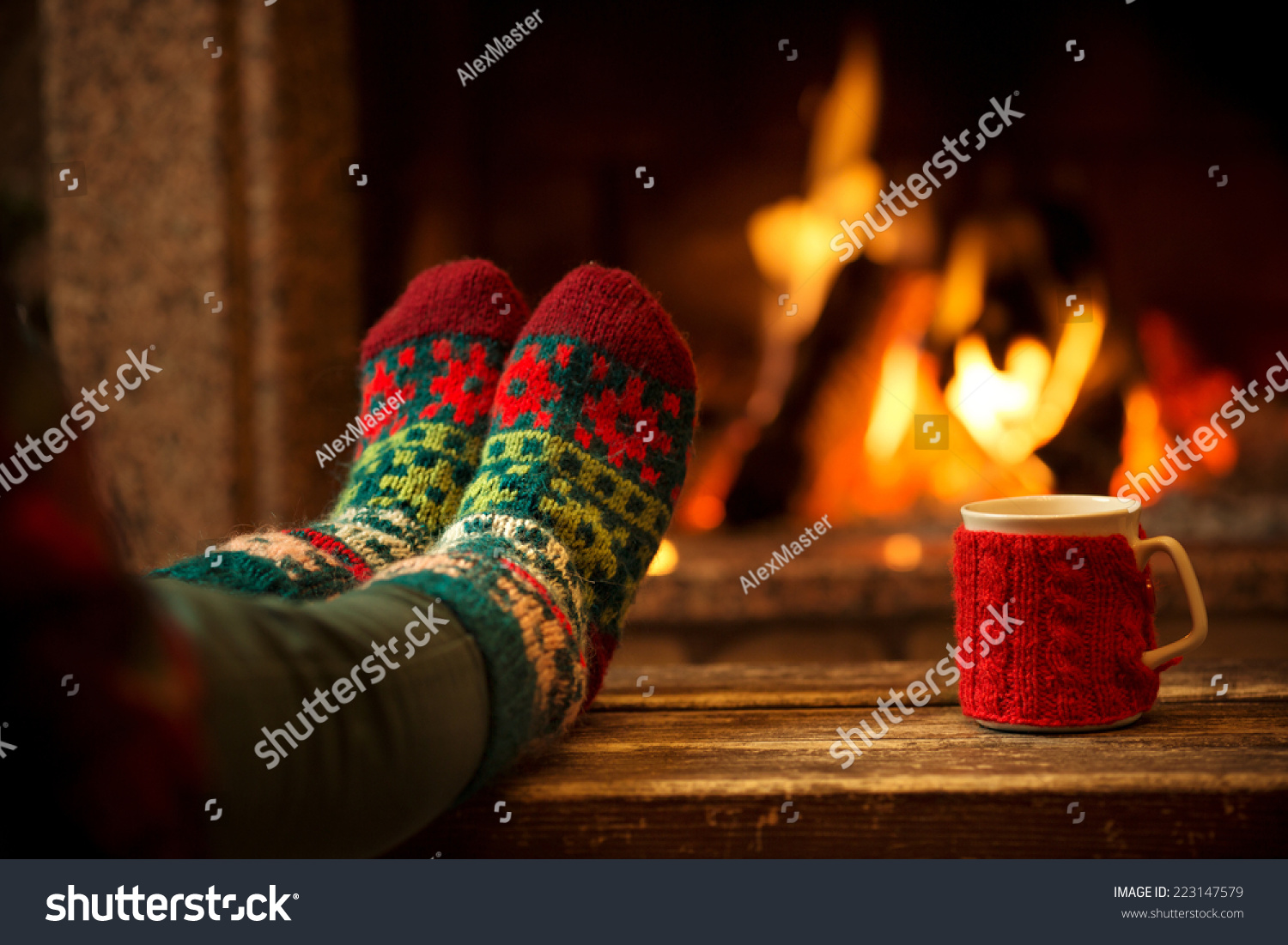 Feet in woollen socks by the Christmas fireplace. Woman relaxes by warm fire with a cup of hot drink and warming up her feet in woollen socks. Close up on feet. Winter and Christmas holidays concept.