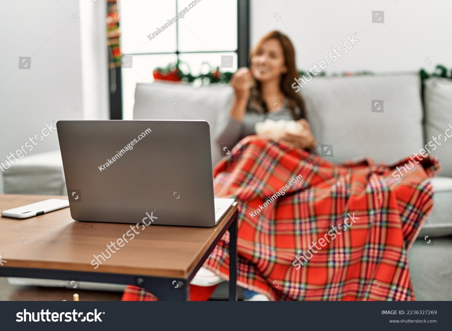 Young latin woman watching movie sitting by christmas decor at home