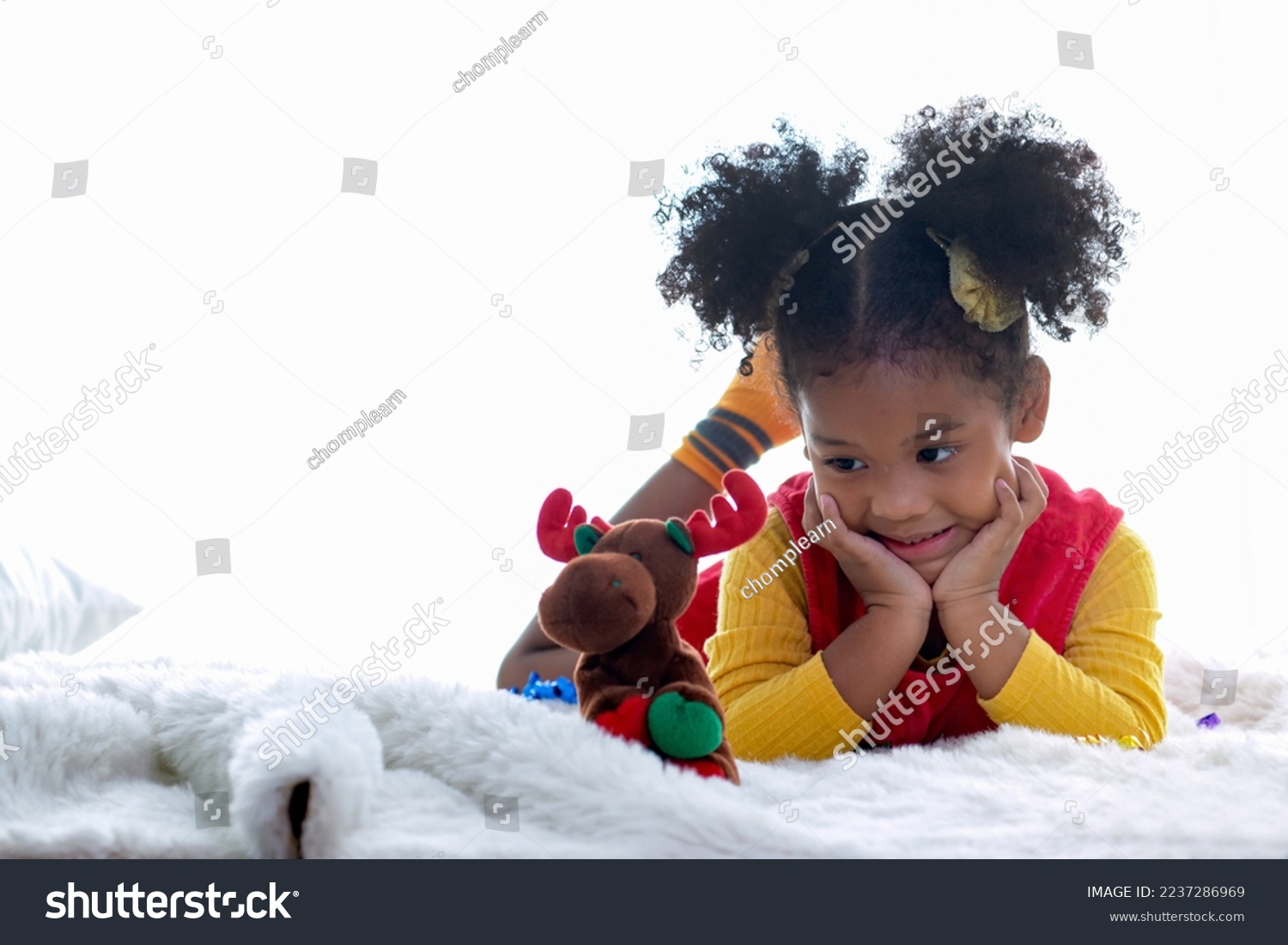 Little cheerful African girl with Christmas toy deer while lying on the bed  playing at home during Christmas time