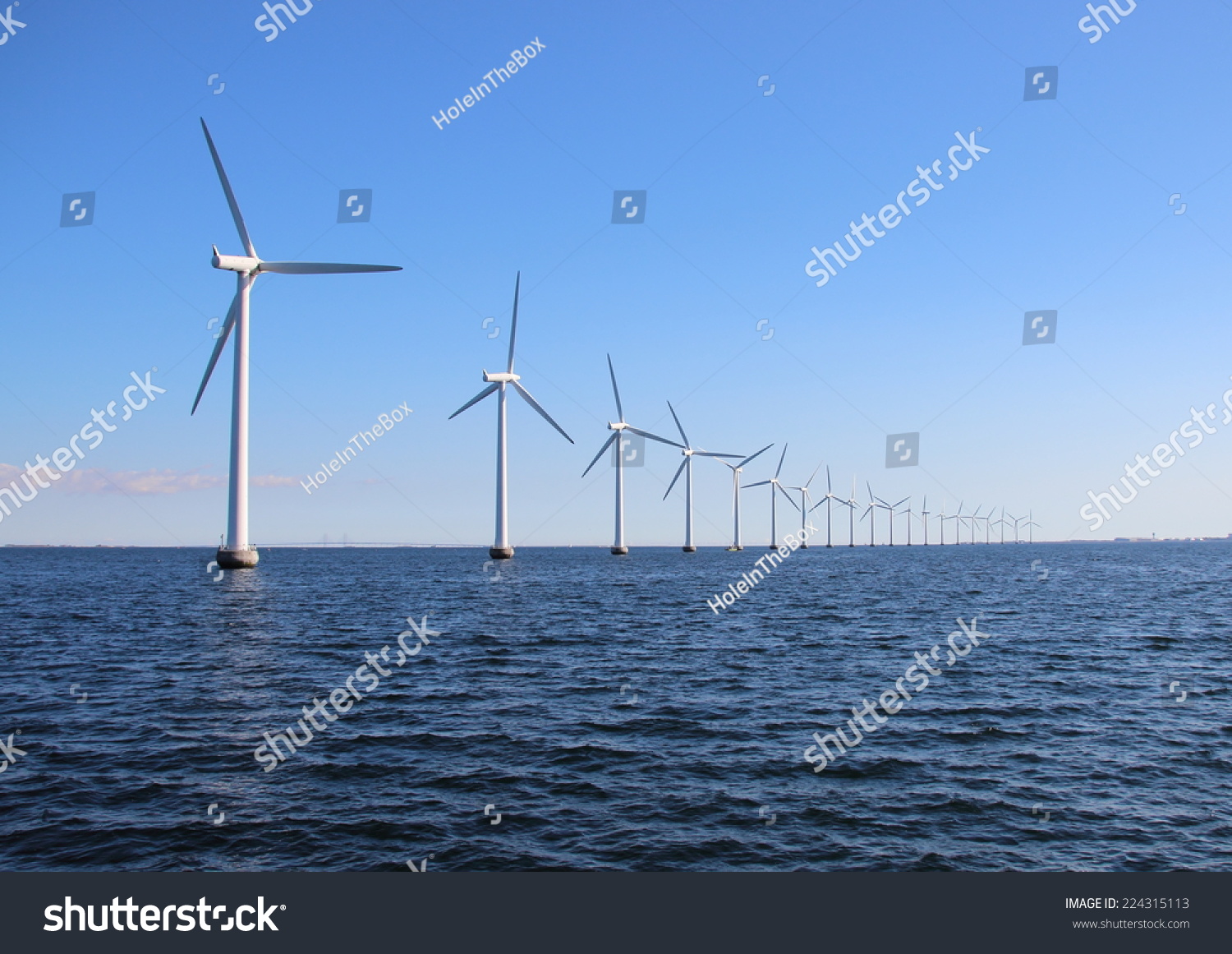 Perspective line of ocean wind mills with dark water and sky