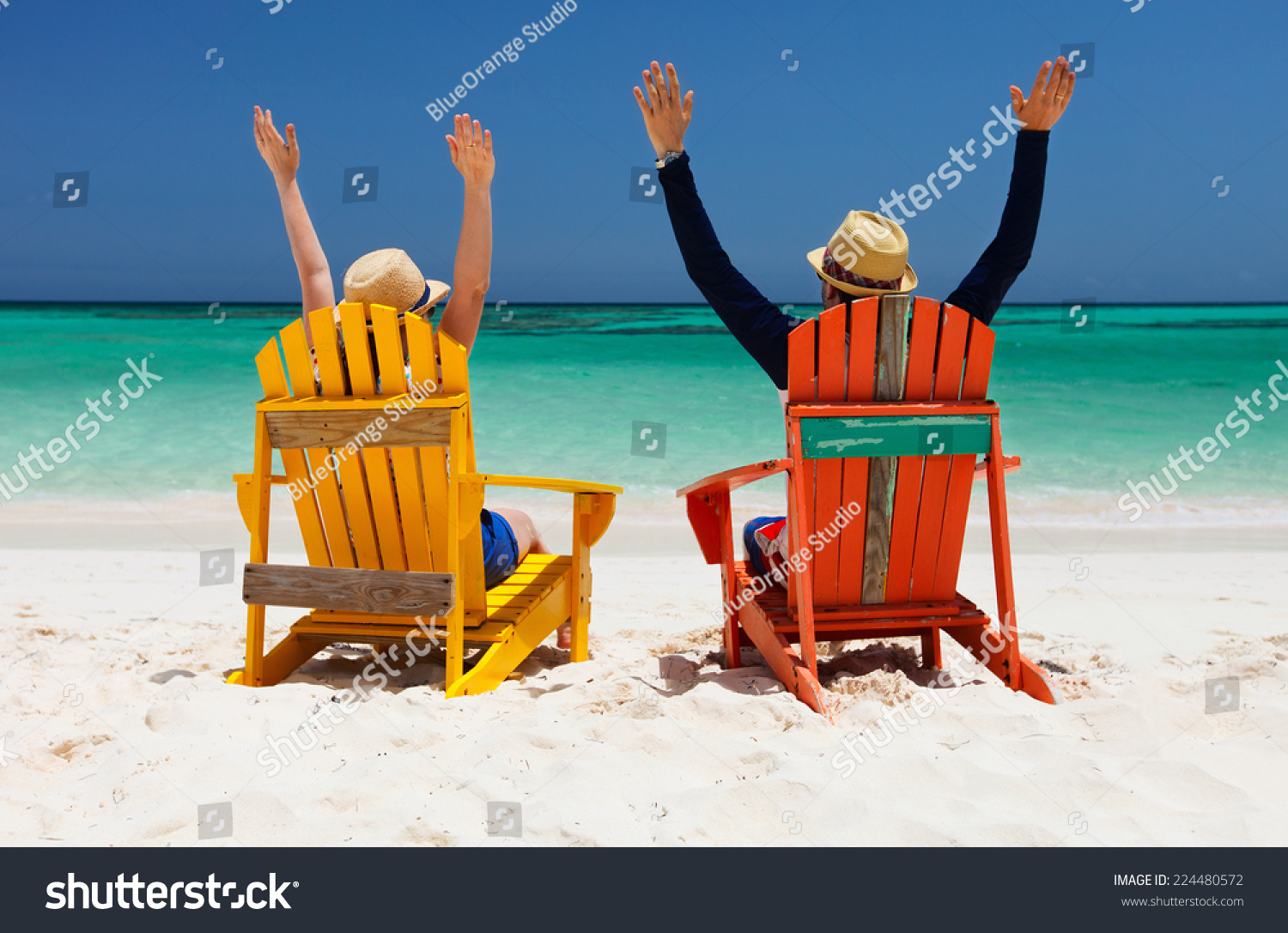 Happy couple sitting on colorful chairs at tropical beach enjoying Caribbean vacation