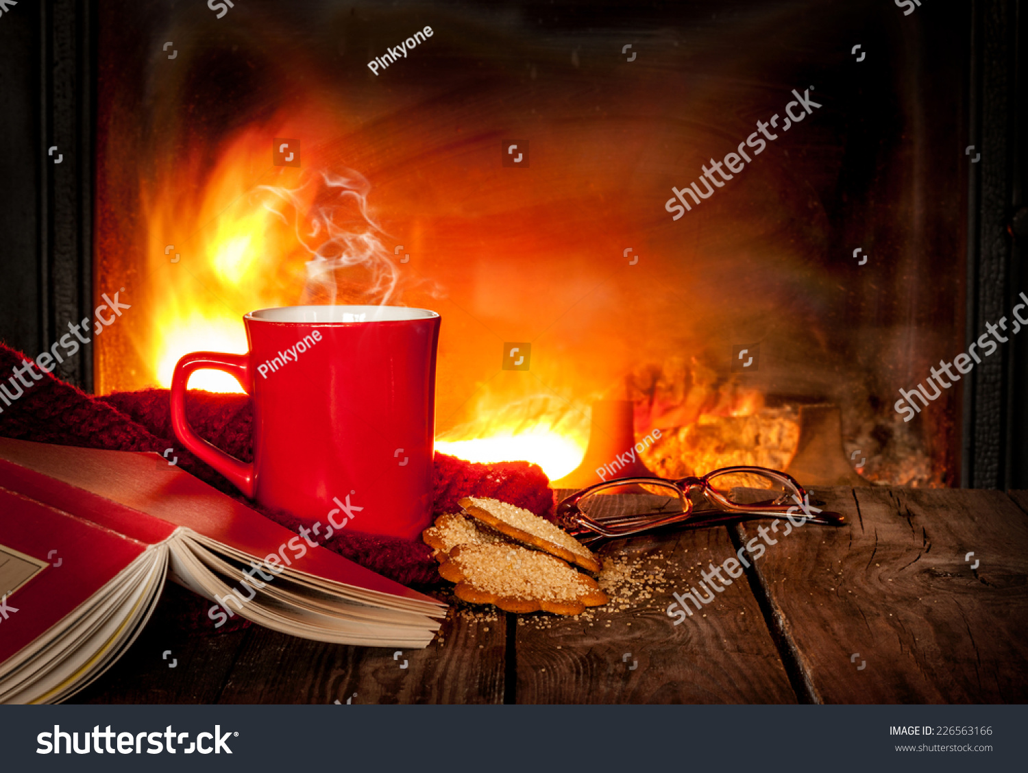 Hot tea or coffee in a red mug ginger cookies book and glasses on vintage wood table. Fireplace as background. Christmas or winter warming drink. Layout with free text space.