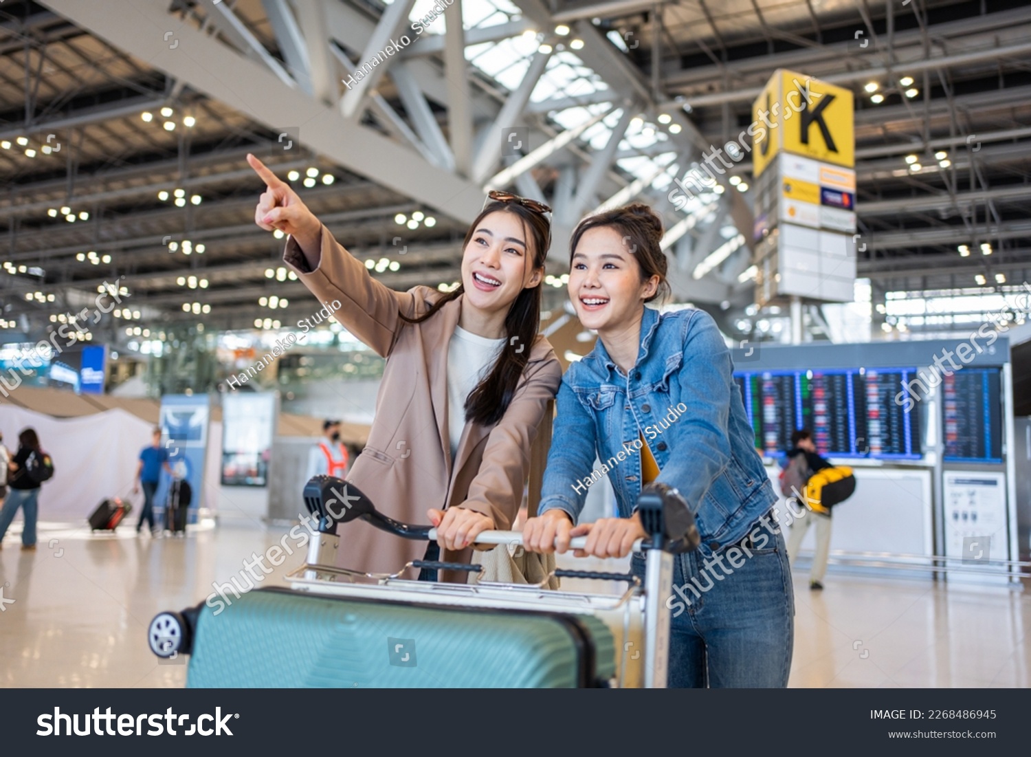 Asian young women passenger walk in airport terminal to boarding gate. Attractive beautiful female tourist friends feeling happy and excited to go travel abroad by airplane for holiday vacation trip.
