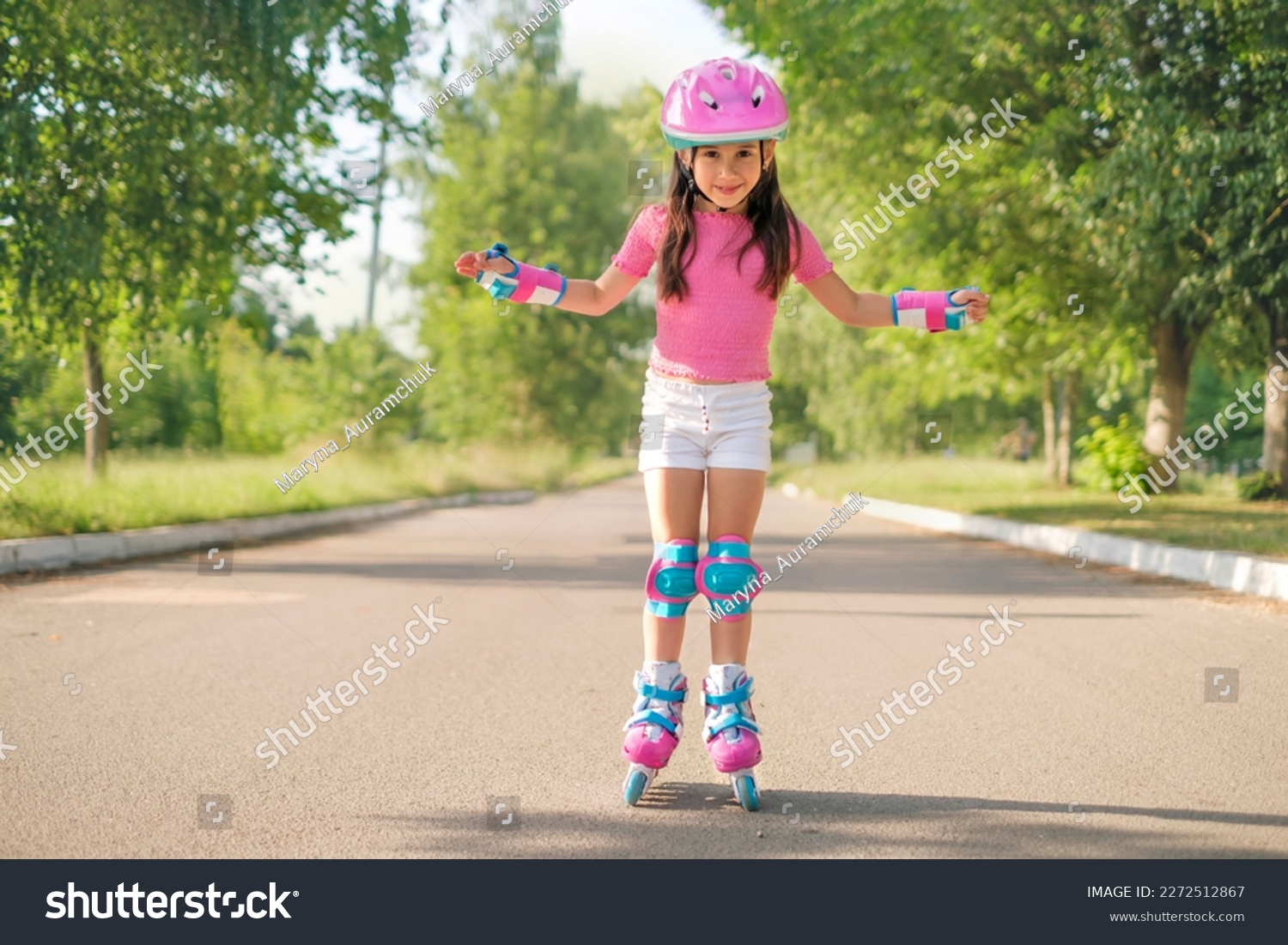 A beautiful preschool girl in a protective sports helmet and roller skates rides on an asphalt path on a hot summer morning.  The child learns new skills and learns sports