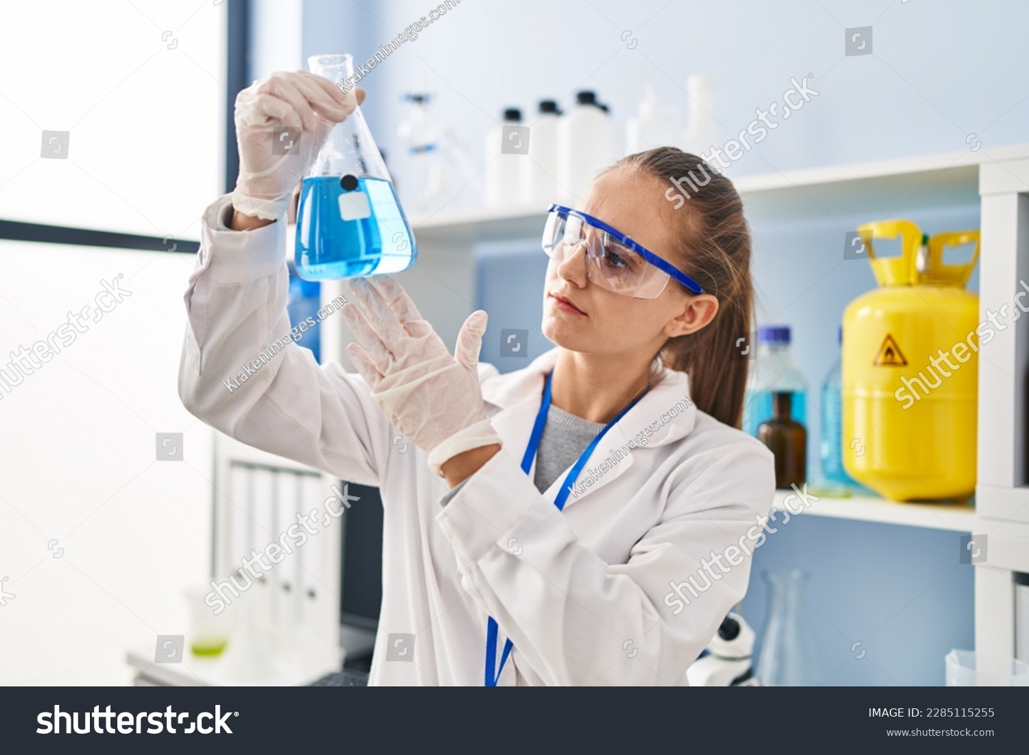 Young blonde woman wearing scientist uniform holding test tube at ...