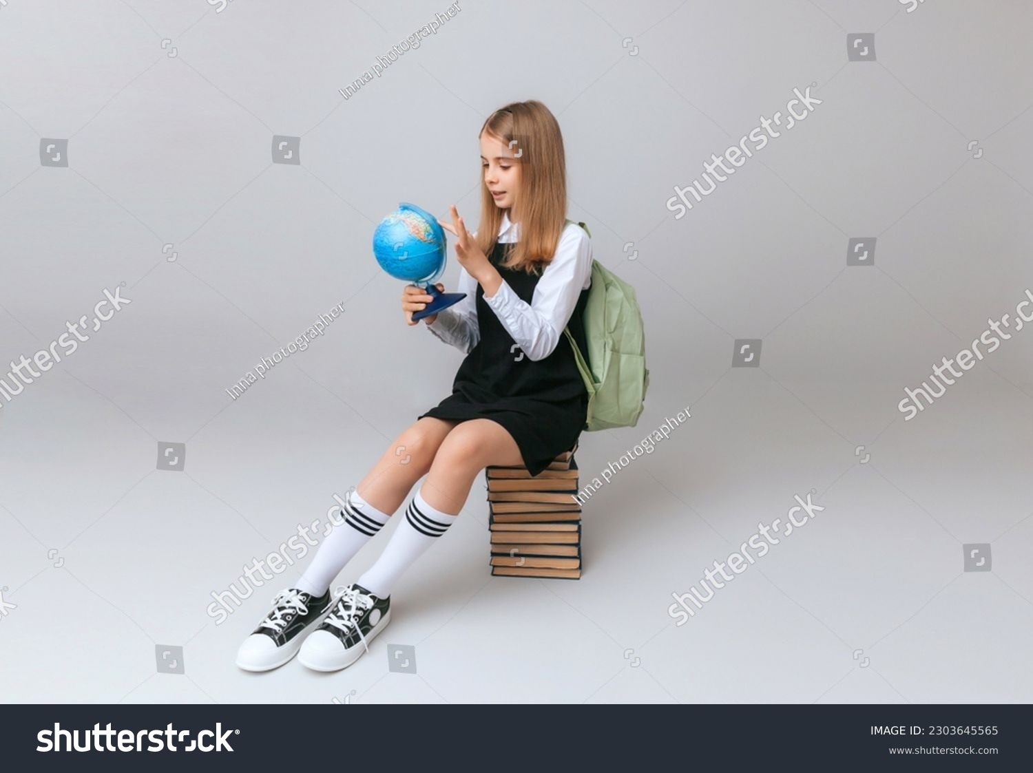 schoolgirl isolated on yellow background with globe. little girl in school uniform sitting on a yellow background reading a book. blonde girl in school uniform on a yellow background