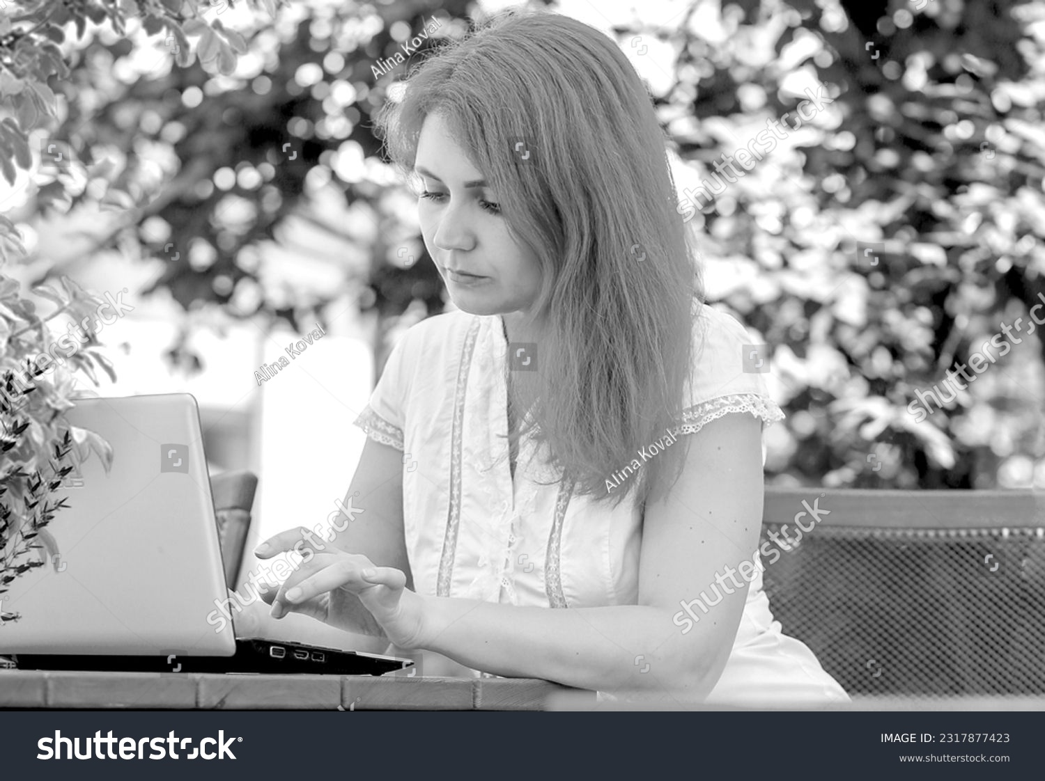 Black and white photo of a young woman working with a laptop in a summer cafe on the street. Coworking. Work outdoors. business concept