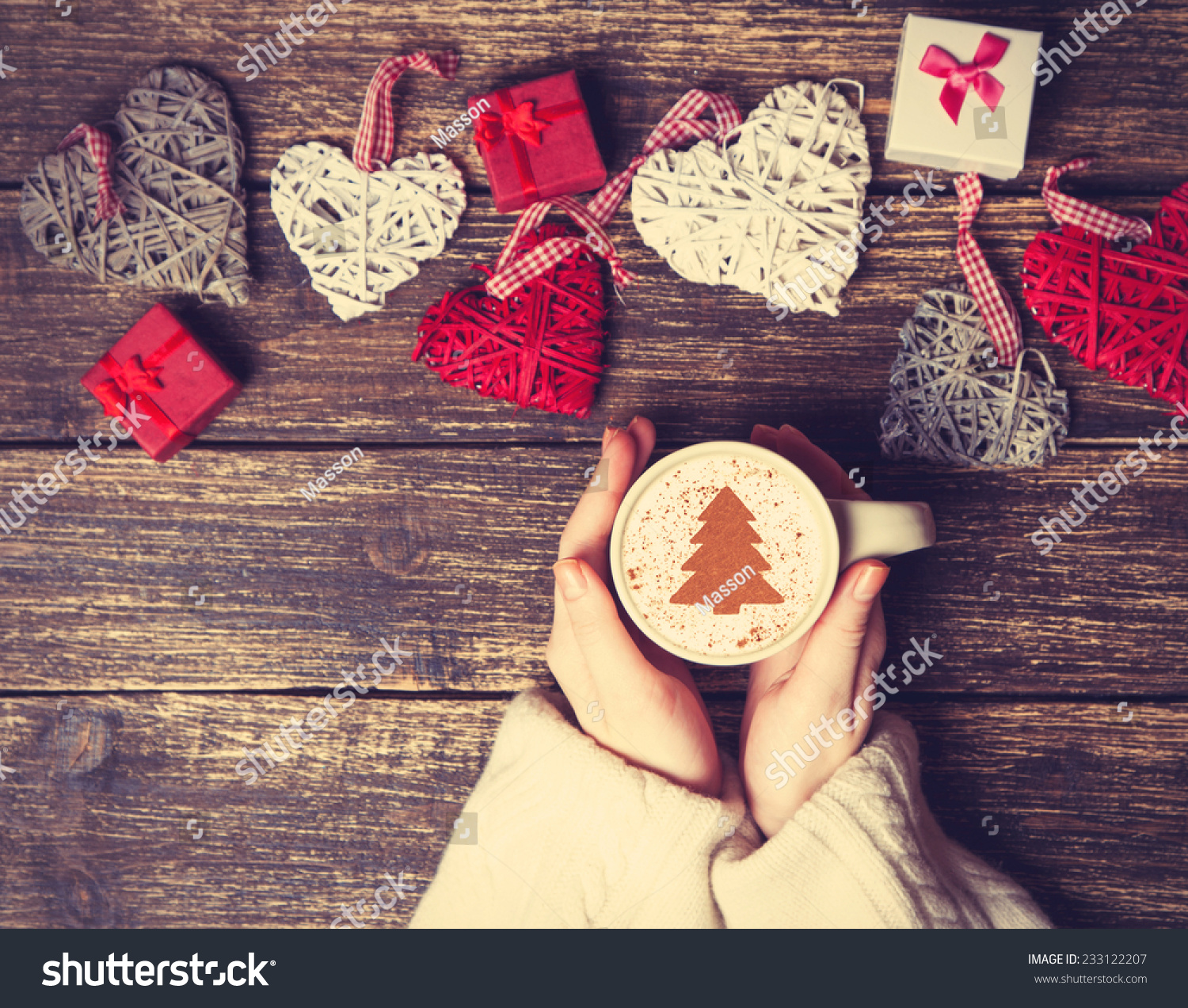 Female holding cup of coffee with cream christmas tree on a table.