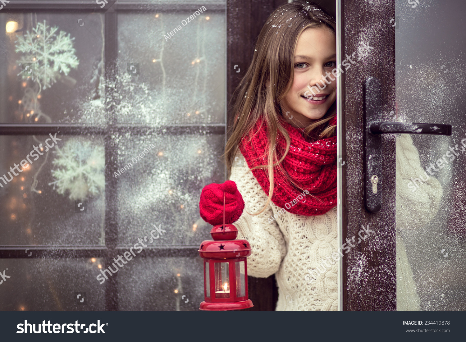 Child girl welcome guests and holding holiday lantern snow weather house is decorated before Christmas