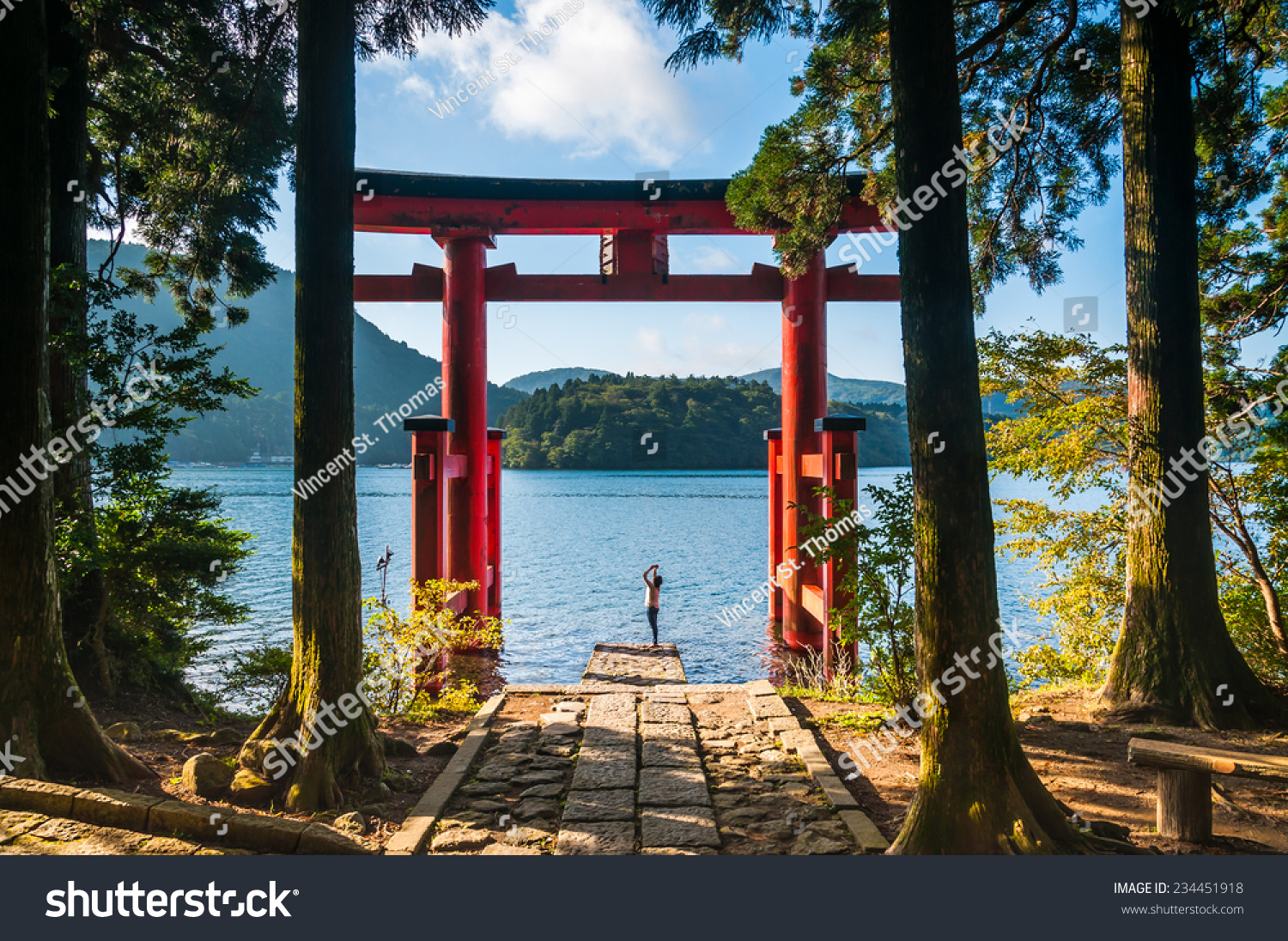 A young woman takes photos with her phone of a torii gate in Hakone  Japan.