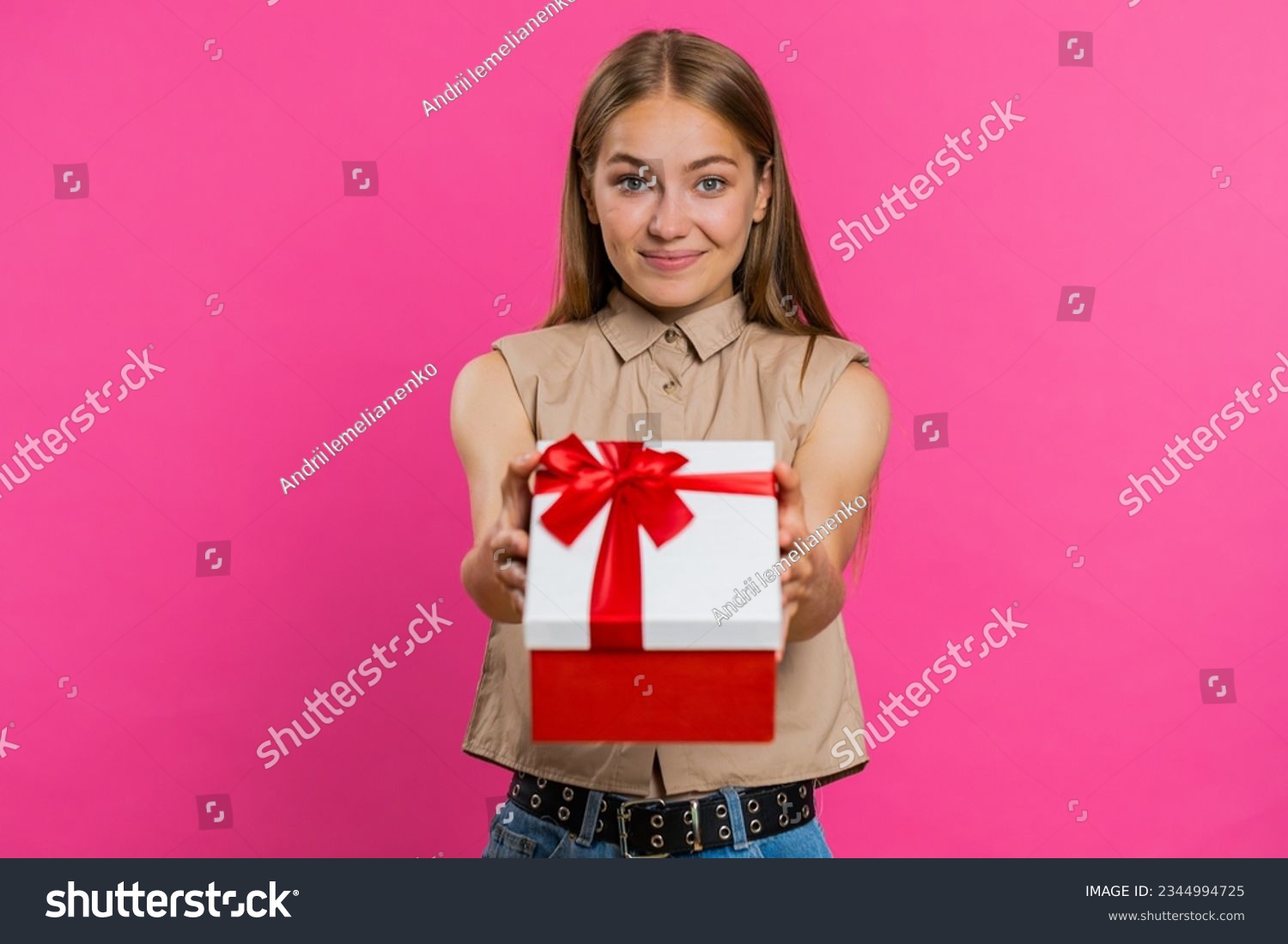 Positive smiling young woman presenting birthday green gift box stretches out hands offer wrapped present career bonus celebrating party sale. Blonde girl isolated alone on pink studio background
