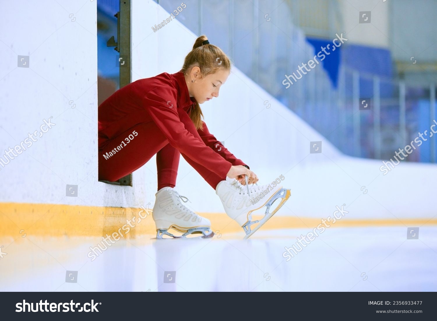 Beautiful girl in red sportswear preparing for training session on ice rink arena  figure skater tying laces on skates. Concept of professional sport  competition  sport school  health  hobby  ad